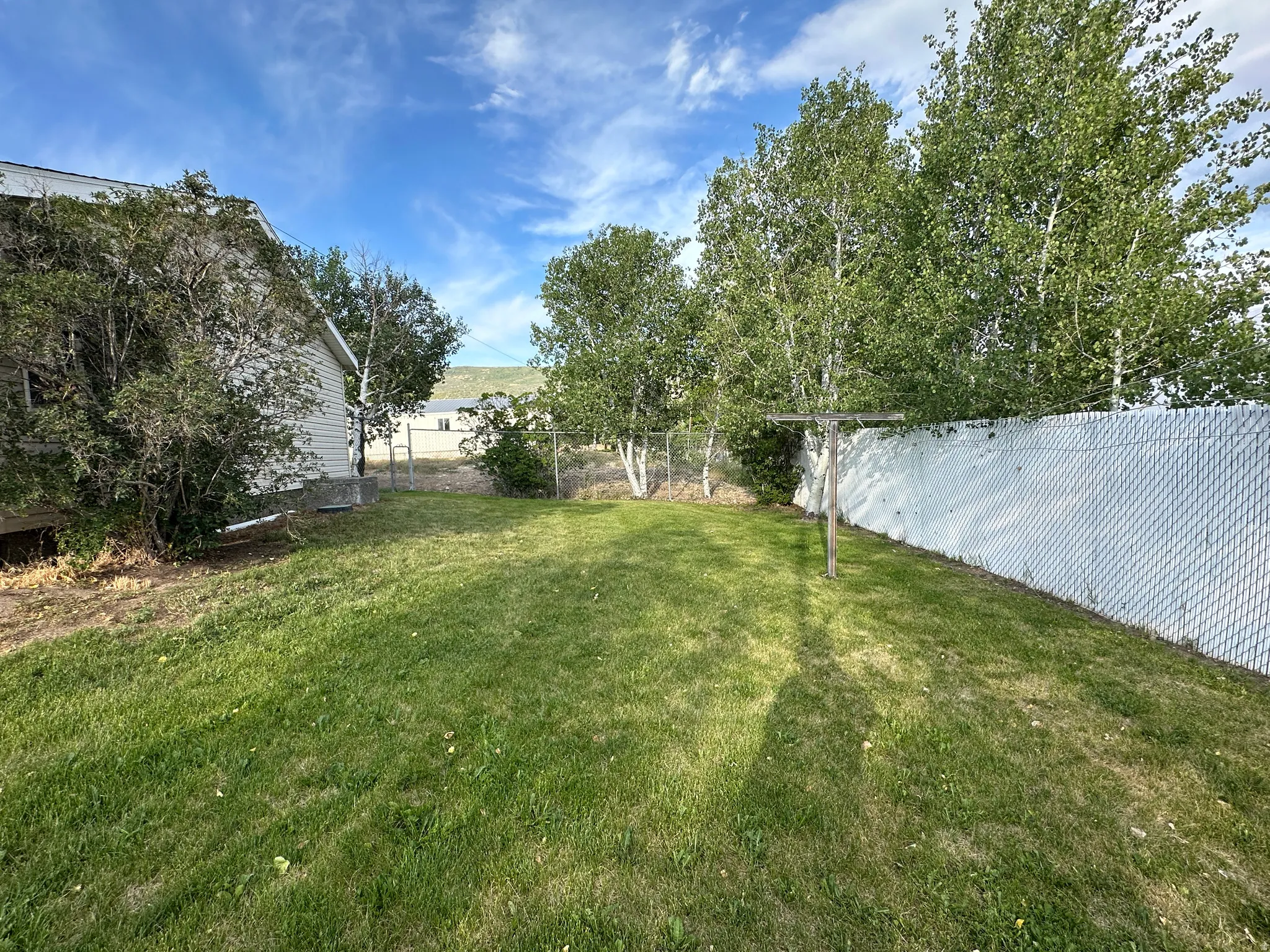 Expansive lawn with mature trees, a white chain-link fence, and a clothesline