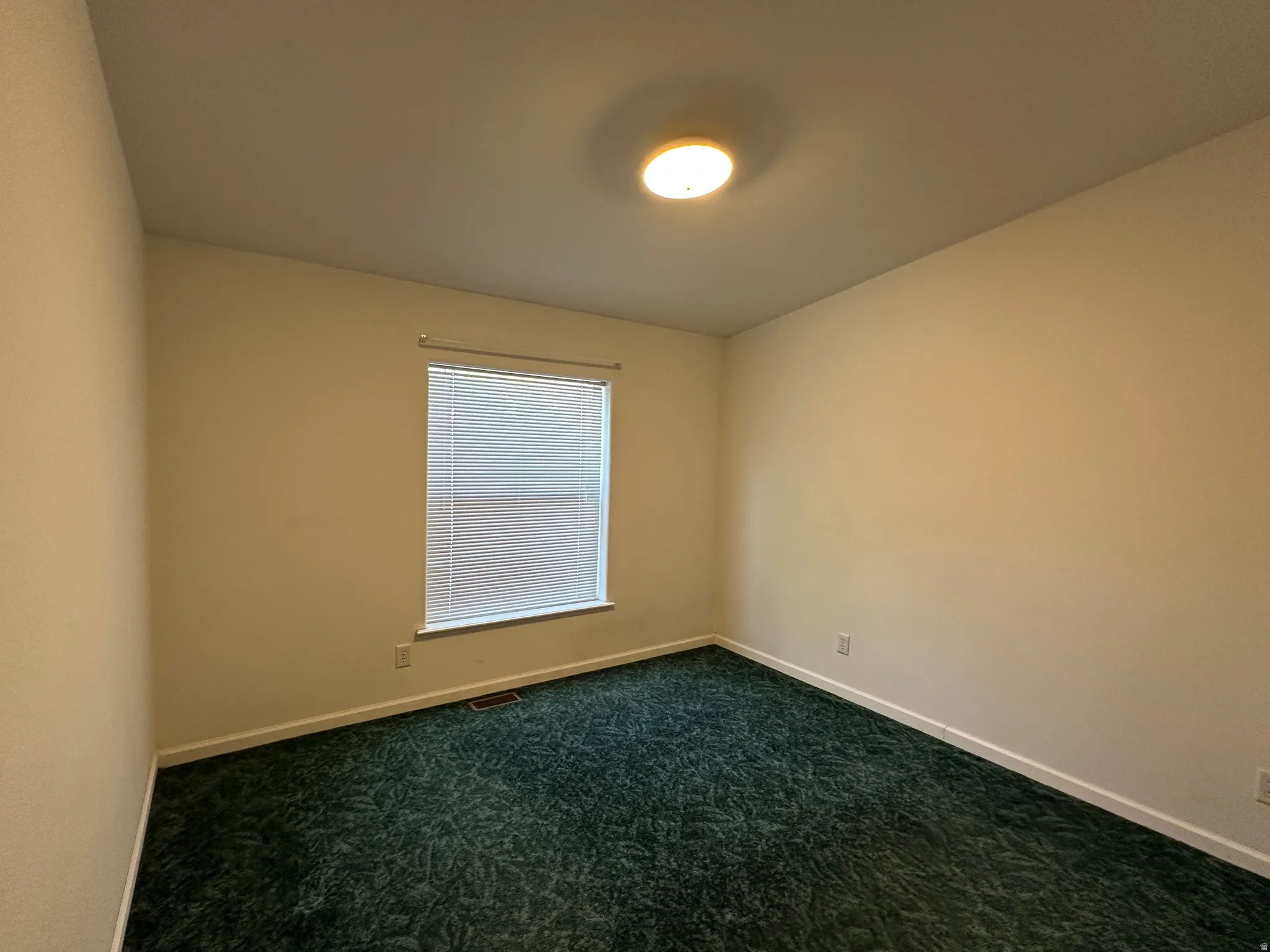 Room featuring neutral tone walls, green patterned carpeting, and a window with horizontal blinds