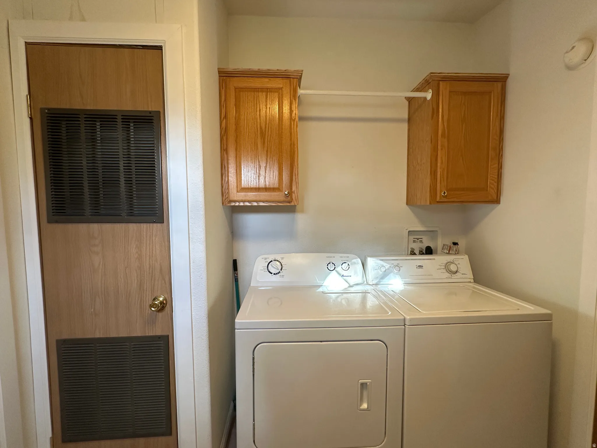 Dedicated laundry area featuring a utility door with ventilation, overhead wood-finish cabinetry, and a clothes hanging rod