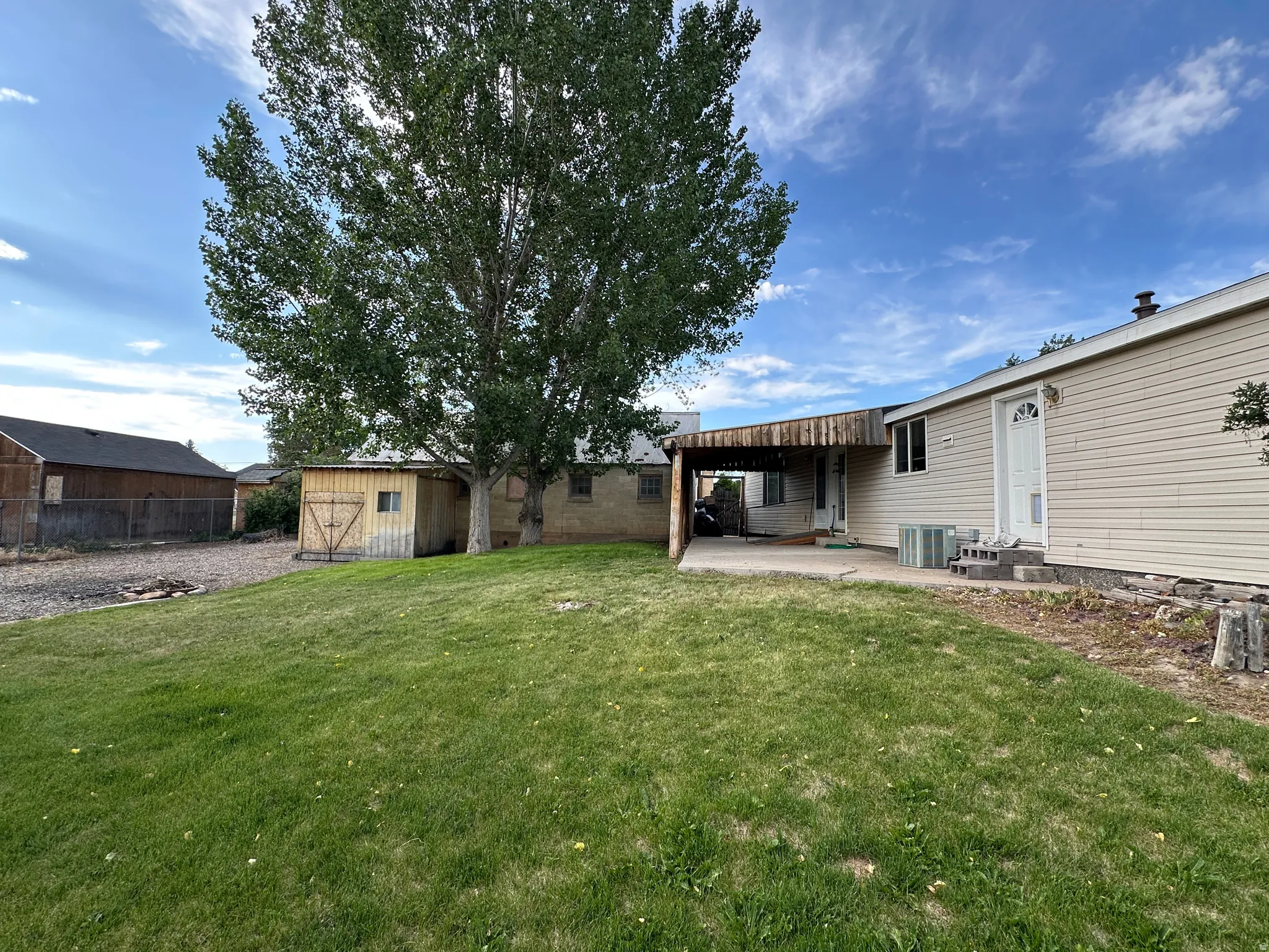 Expansive rear yard featuring a grass lawn, mature shade tree, and wood-sided shed