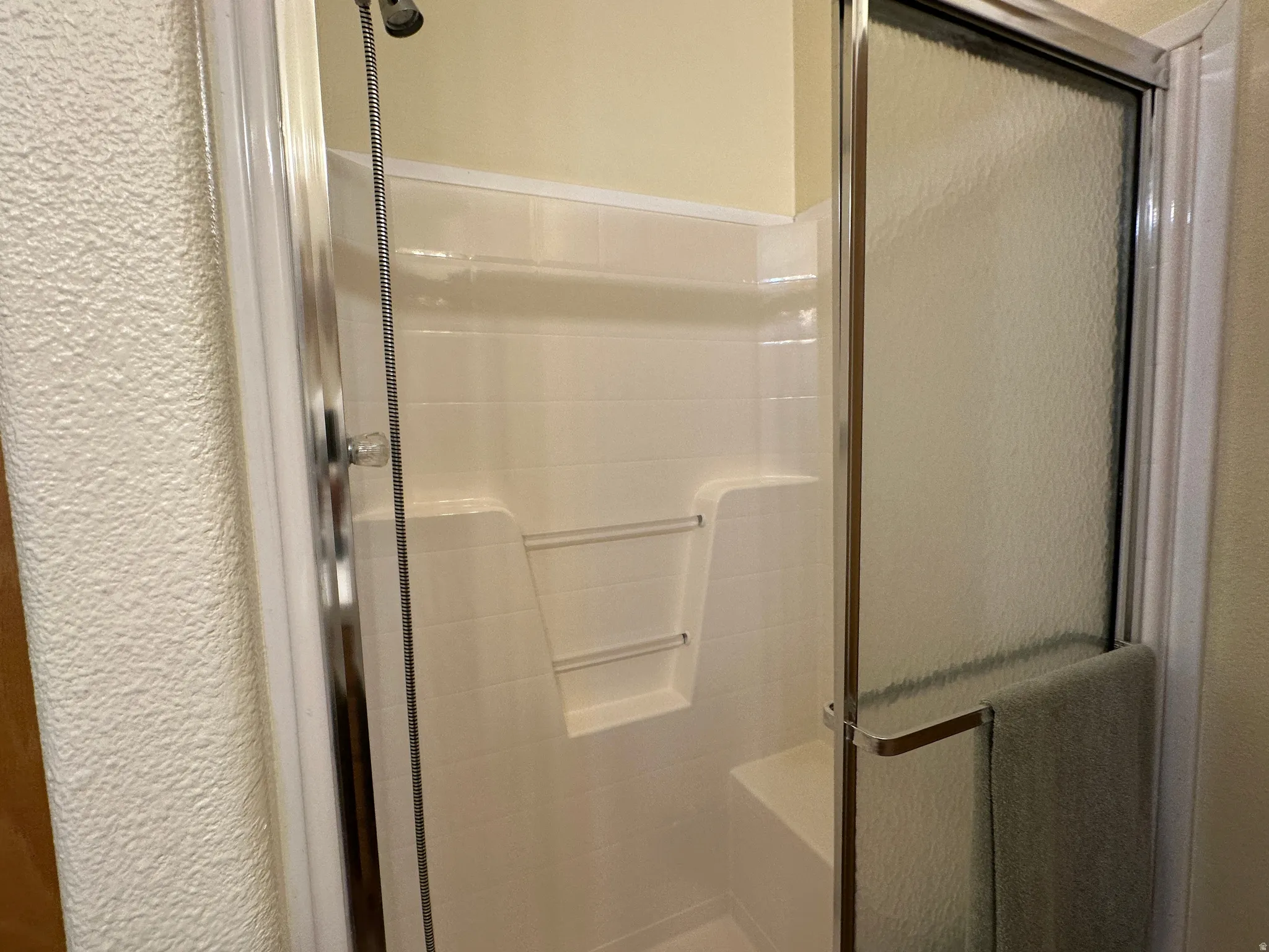 Enclosed shower with a textured glass door, integrated seating, and built-in shelving