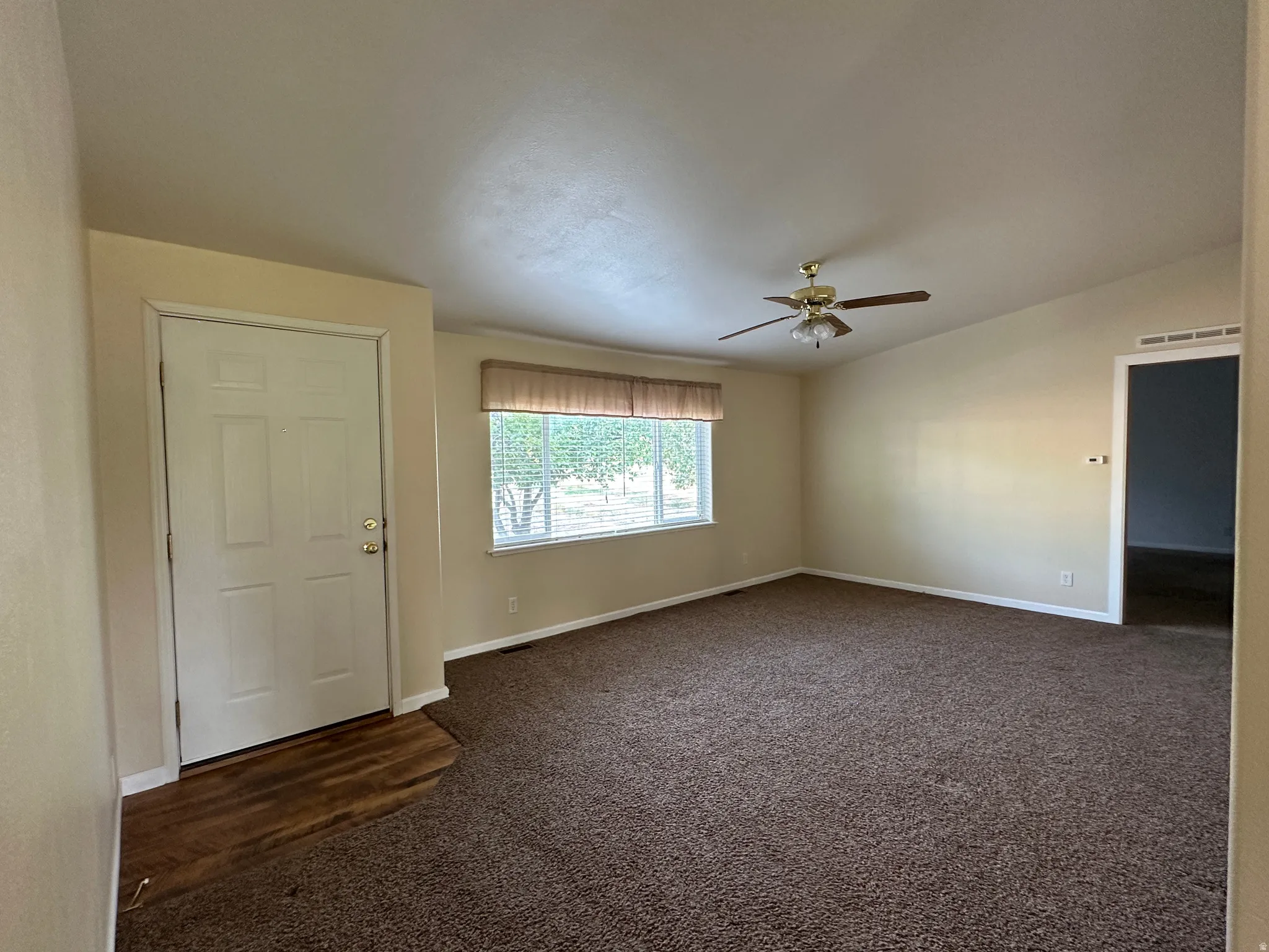 Spacious living area featuring neutral-toned walls, vaulted ceilings, and a ceiling fan with light fixture
