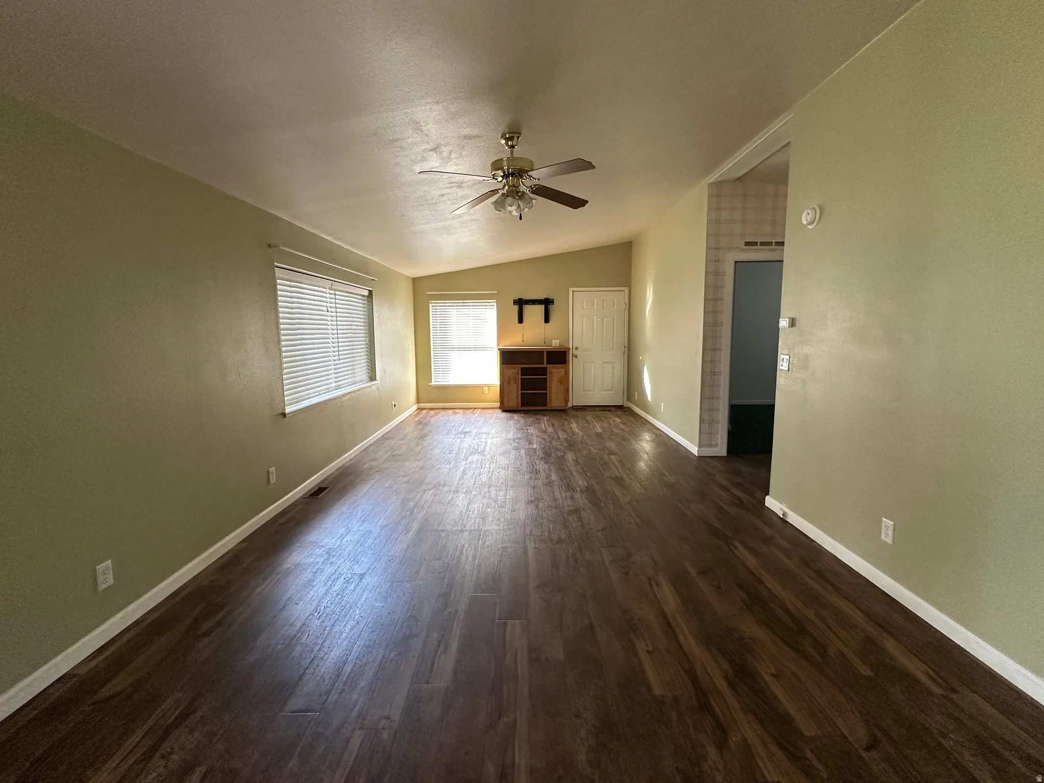 Spacious interior featuring wood-finish flooring, vaulted ceiling, and multiple windows with blinds