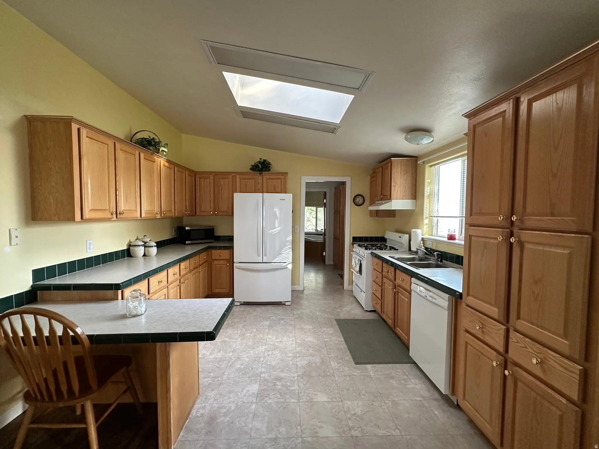 Kitchen featuring extensive wood cabinetry, L-shaped countertops with green tile backsplash, built-in breakfast bar, and skylight