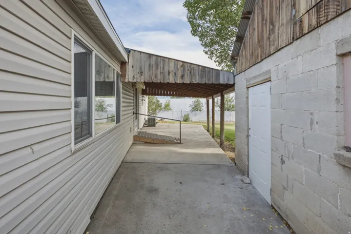 Side exterior featuring beige horizontal siding, multiple windows, an extended covered patio, concrete block construction, and a white entry door