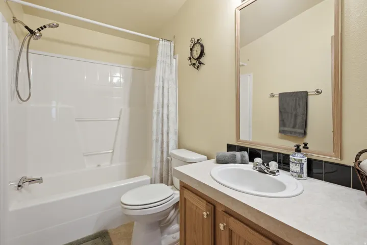 Bathroom featuring a white tub and shower combination with a curved shower curtain rod, a wood-finish vanity with an integrated sink, a light-toned countertop