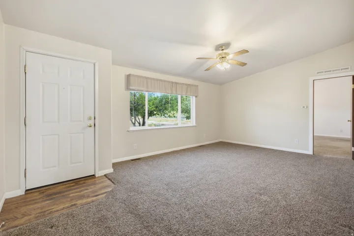 Spacious room featuring vaulted ceilings, a ceiling fan with integrated lighting, and a large window with privacy valance, with front door entrance area.