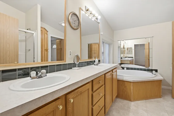 Dual sink vanity with laminate countertops and wood cabinetry with large tub