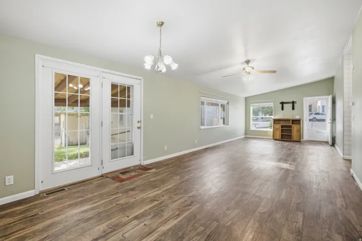 Spacious room featuring wood-finish flooring, vaulted ceilings, and a neutral wall color, with doors to back covered patio area.