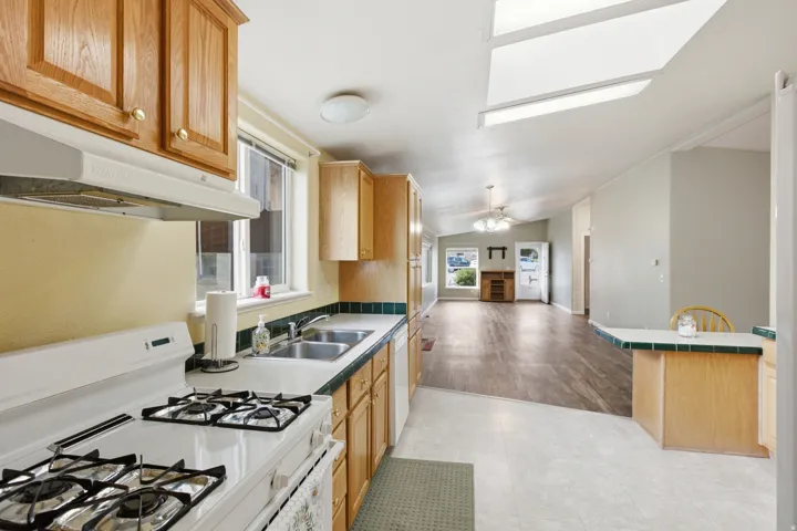 Kitchen with wood cabinetry, white appliances, a double basin sink, and a tiled countertop