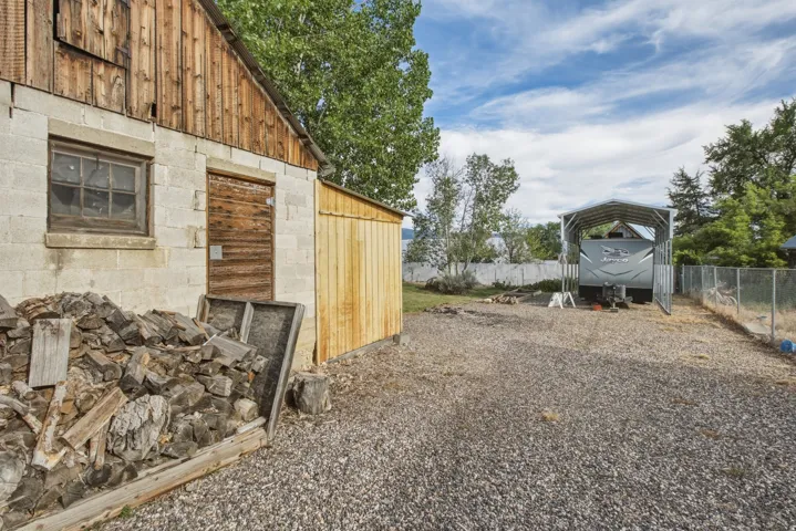 Gravel driveway featuring a large metal carport structure, and wood pile for the fire ring