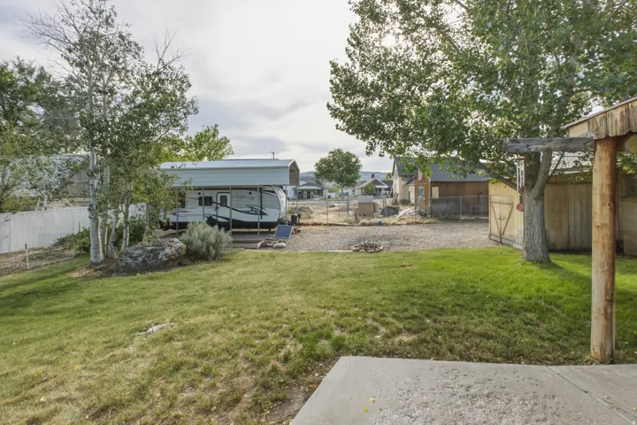 Expansive backyard featuring a concrete patio slab, mature trees, a storage shed, and a gravel pad area with covered rv parking.