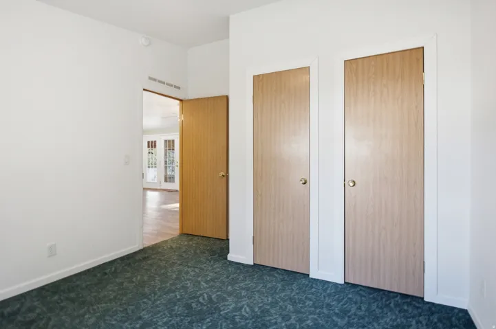 Bedroom with  two closet doors, a white wall, and patterned green carpeting