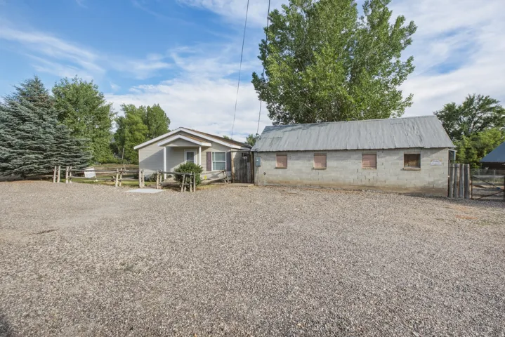 Gravel driveway with a house featuring a covered front porch, a wood fence, and mature trees