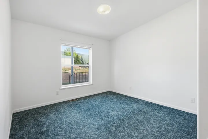 Bright Bedroom #2 featuring a window with exterior views, white walls, and blue patterned carpeting