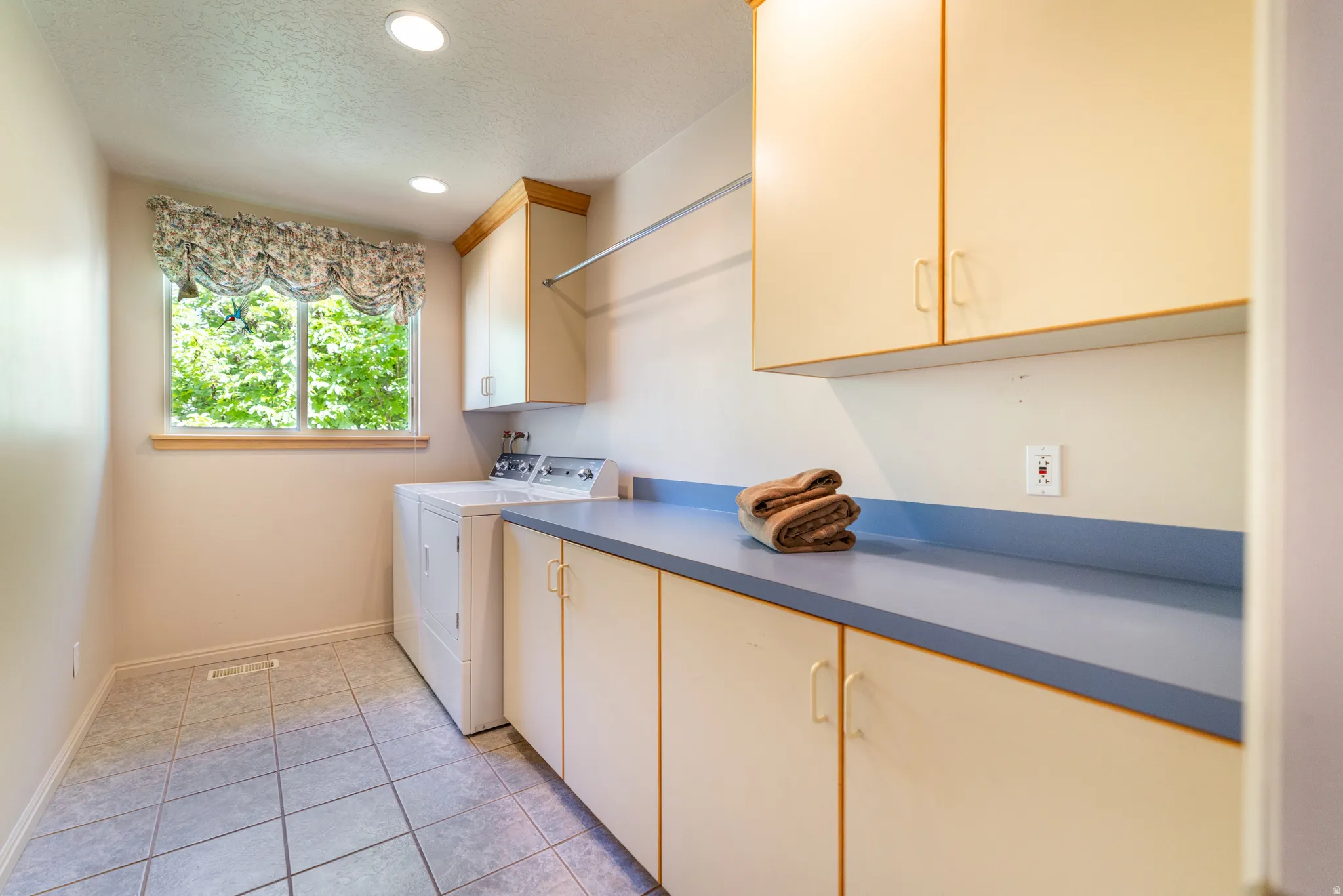 Dedicated laundry room featuring tile flooring, a large window, recessed lighting, ample cabinetry, and a spacious countertop