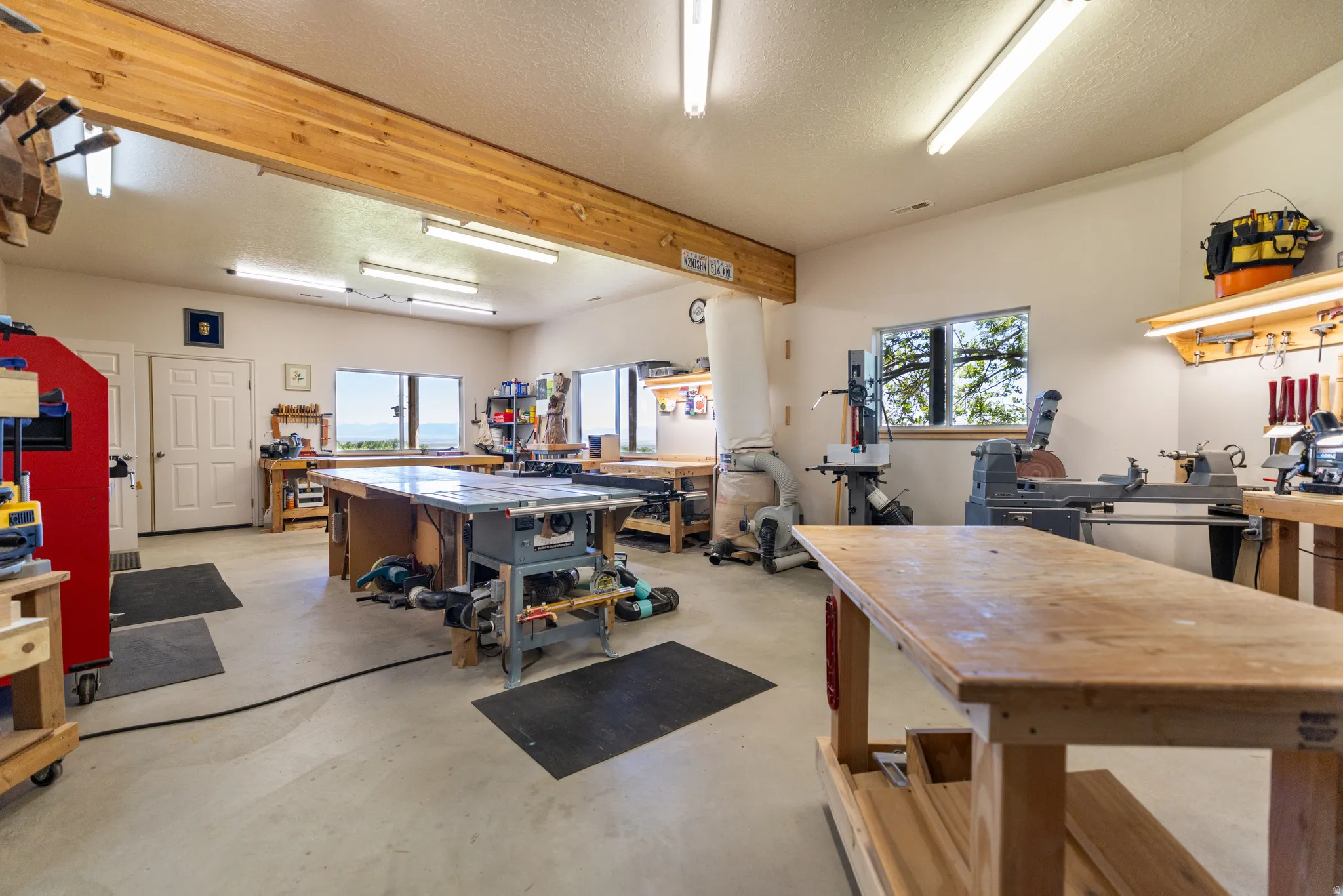 Spacious workshop featuring multiple workbenches, overhead fluorescent lighting, and large windows