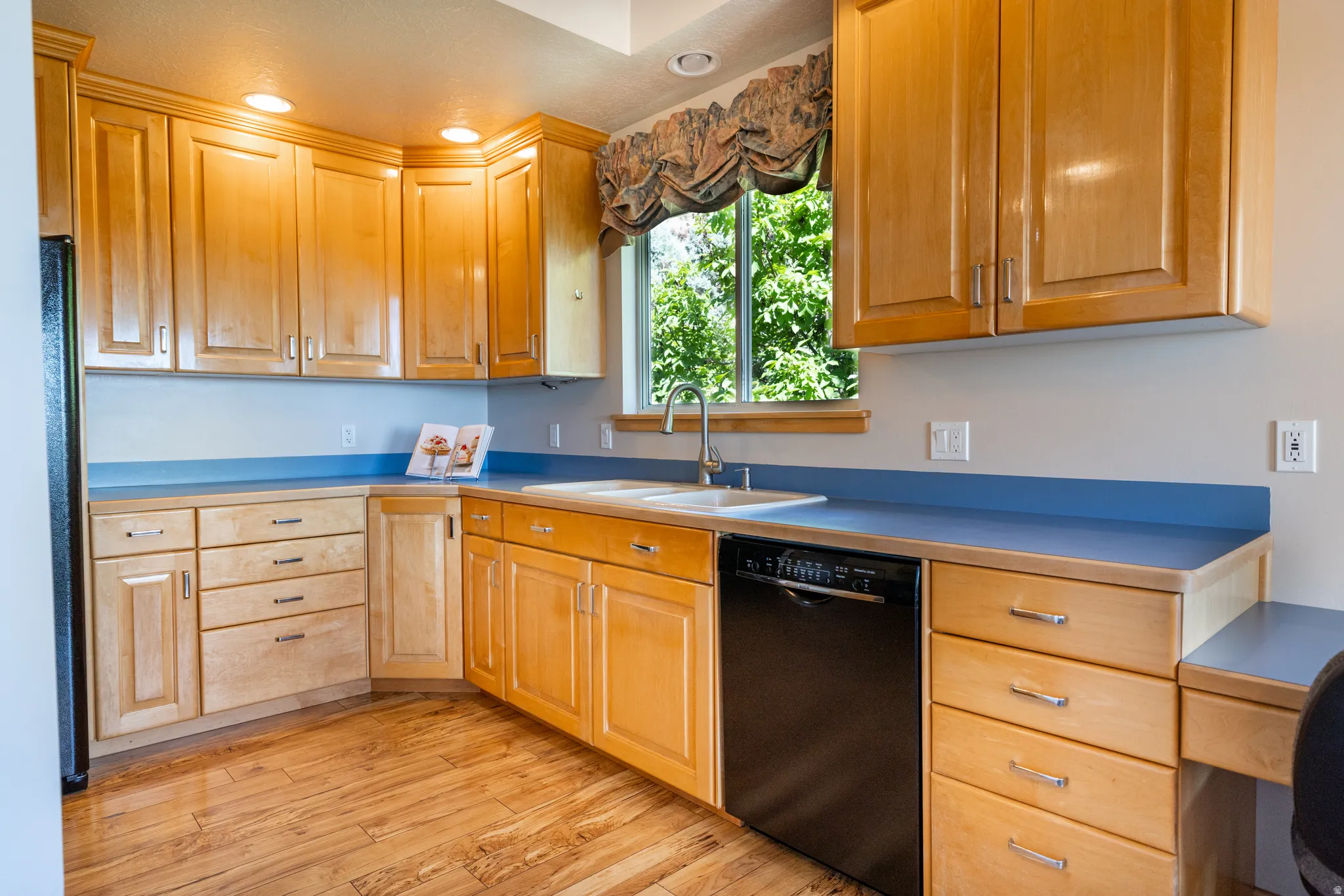 Wood-finish flooring anchors this kitchen featuring extensive light wood cabinetry, recessed lighting, and blue countertops