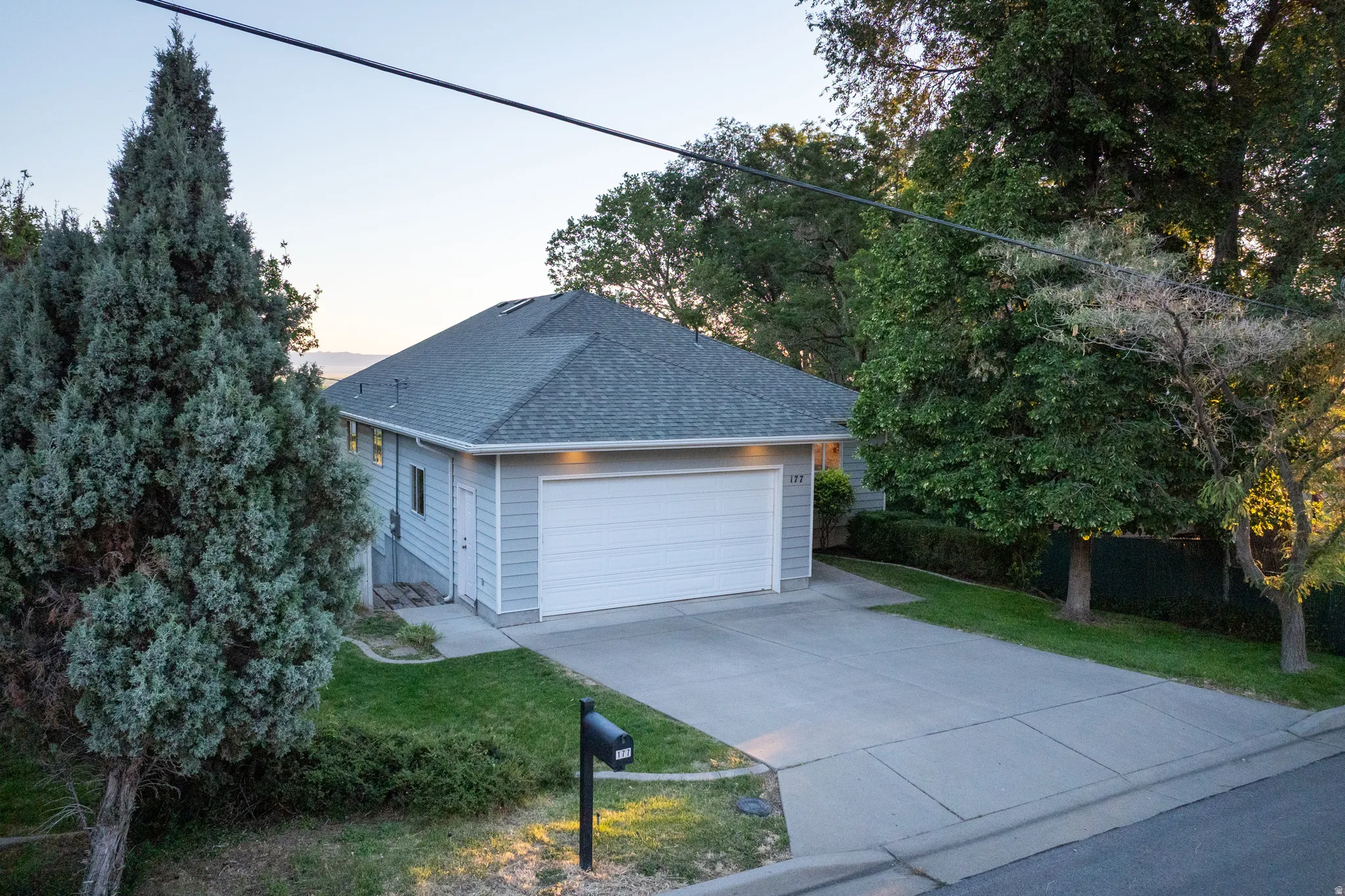 Light gray siding residence with an attached two-car garage, concrete driveway, and a dark gray shingle roof