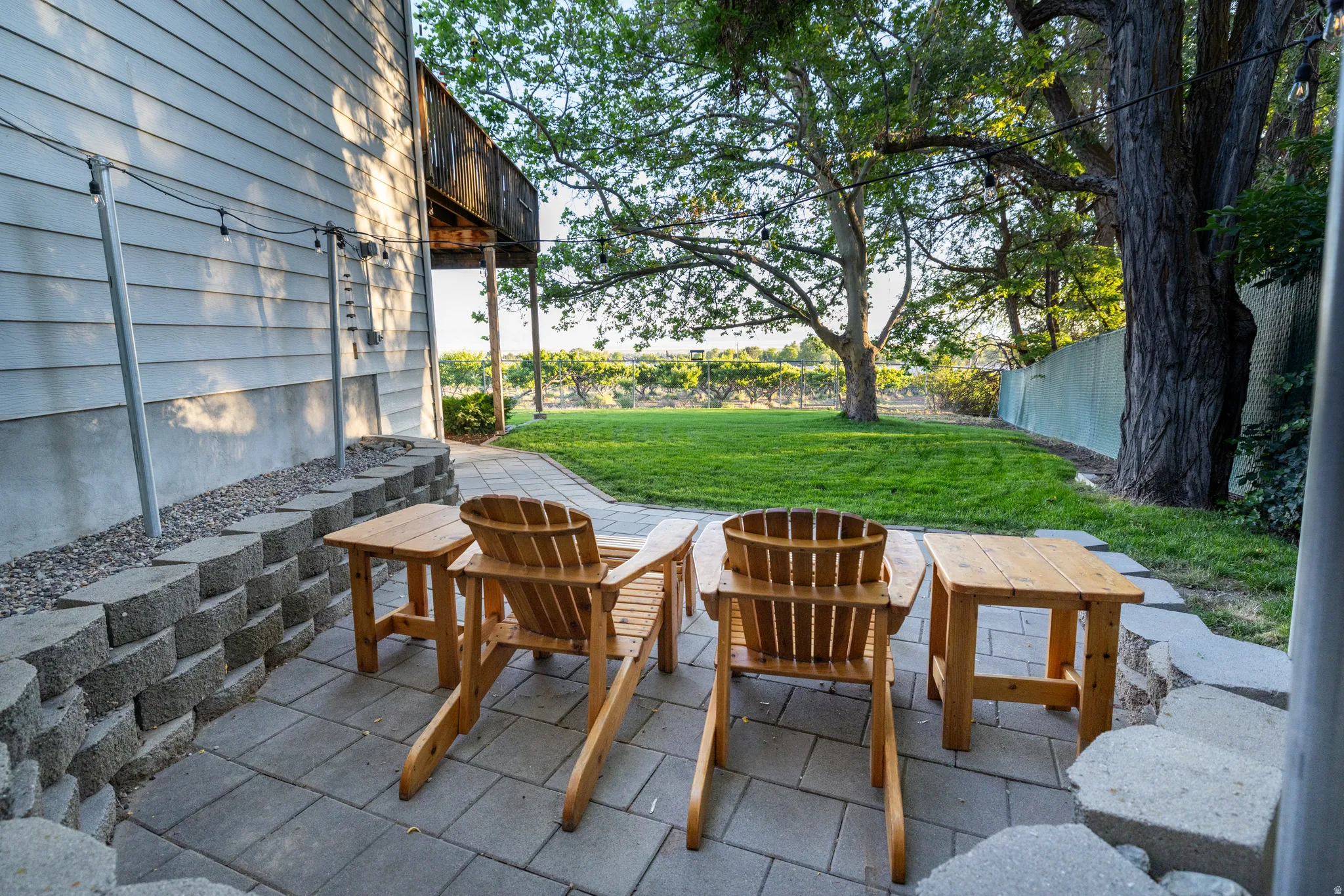 Paver patio with a stacked block retaining wall, manicured lawn, and mature trees