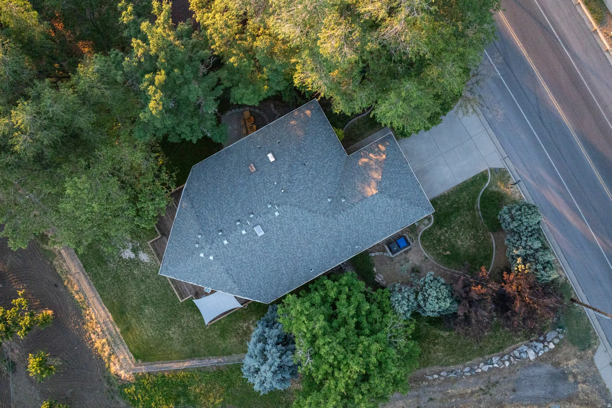 Aerial view showcasing the property's main residence with a gray shingle roof, surrounded by mature trees