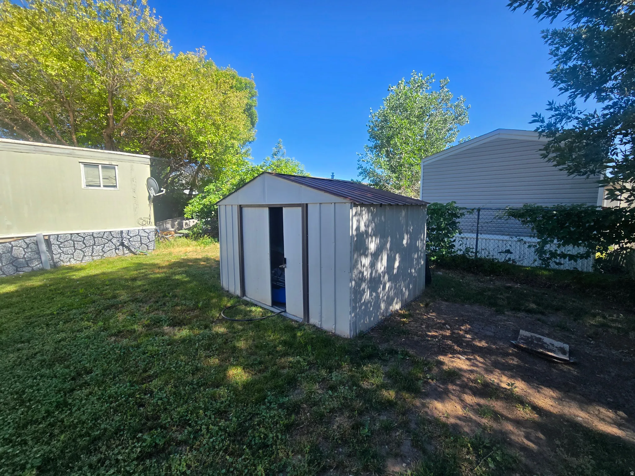 Detached storage shed with a metal roof and light-colored siding, situated on a grass and dirt patch