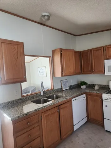 Kitchen featuring wood cabinetry, granite-style countertops, double stainless steel sink, and white appliances