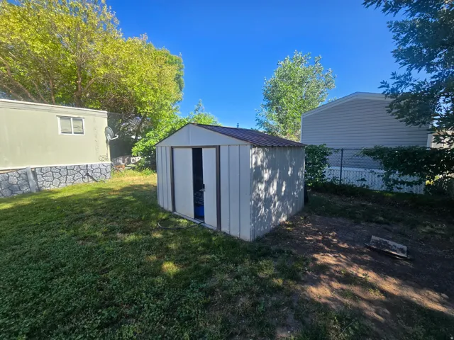 Detached storage shed with a metal roof and light-colored siding, situated on a grass and dirt patch
