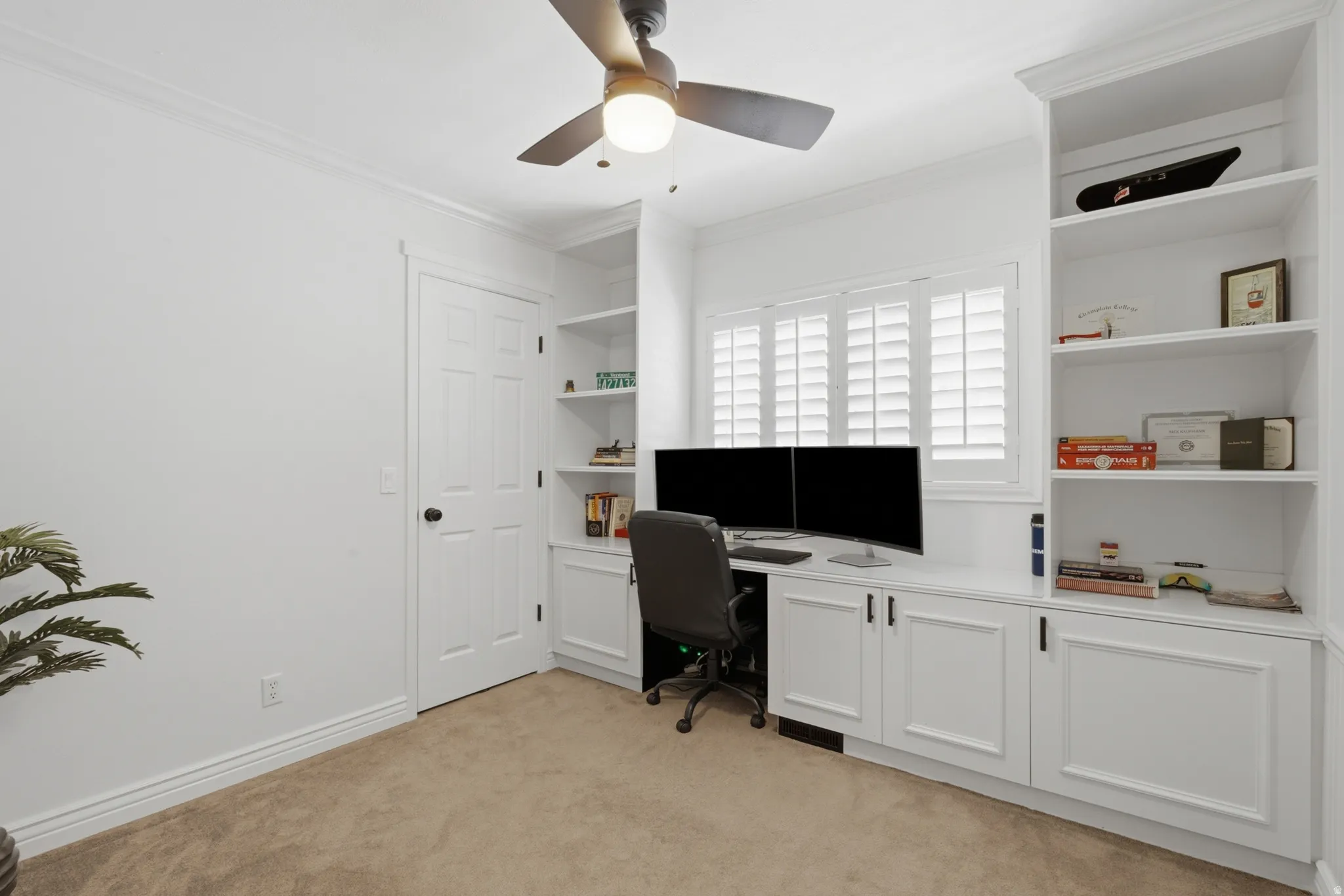 Built-in desk area featuring white cabinetry with black hardware, integrated shelving, and a window with white plantation shutters