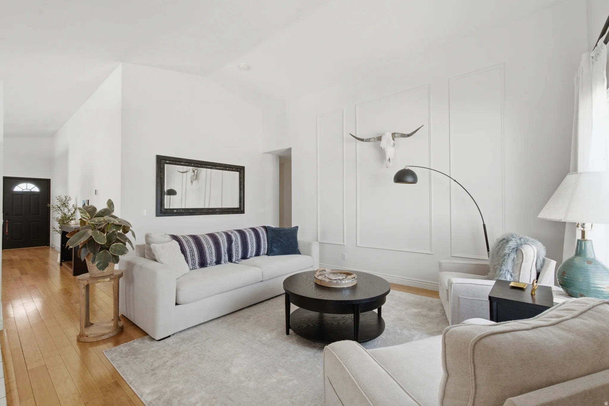 Vaulted ceiling living room featuring wainscoting accent walls, wood-finish flooring, and a semi-circular transom entry door