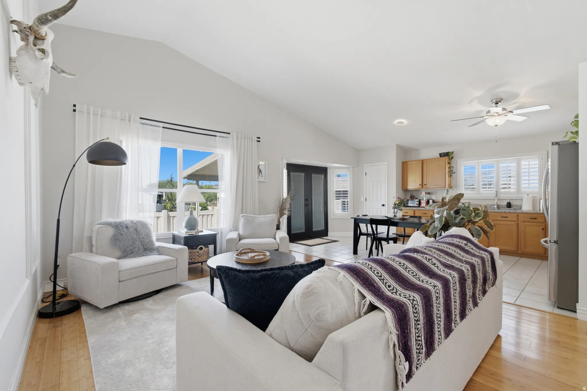 Spacious living area featuring vaulted ceilings, wood-finish flooring, and large windows with white sheers
