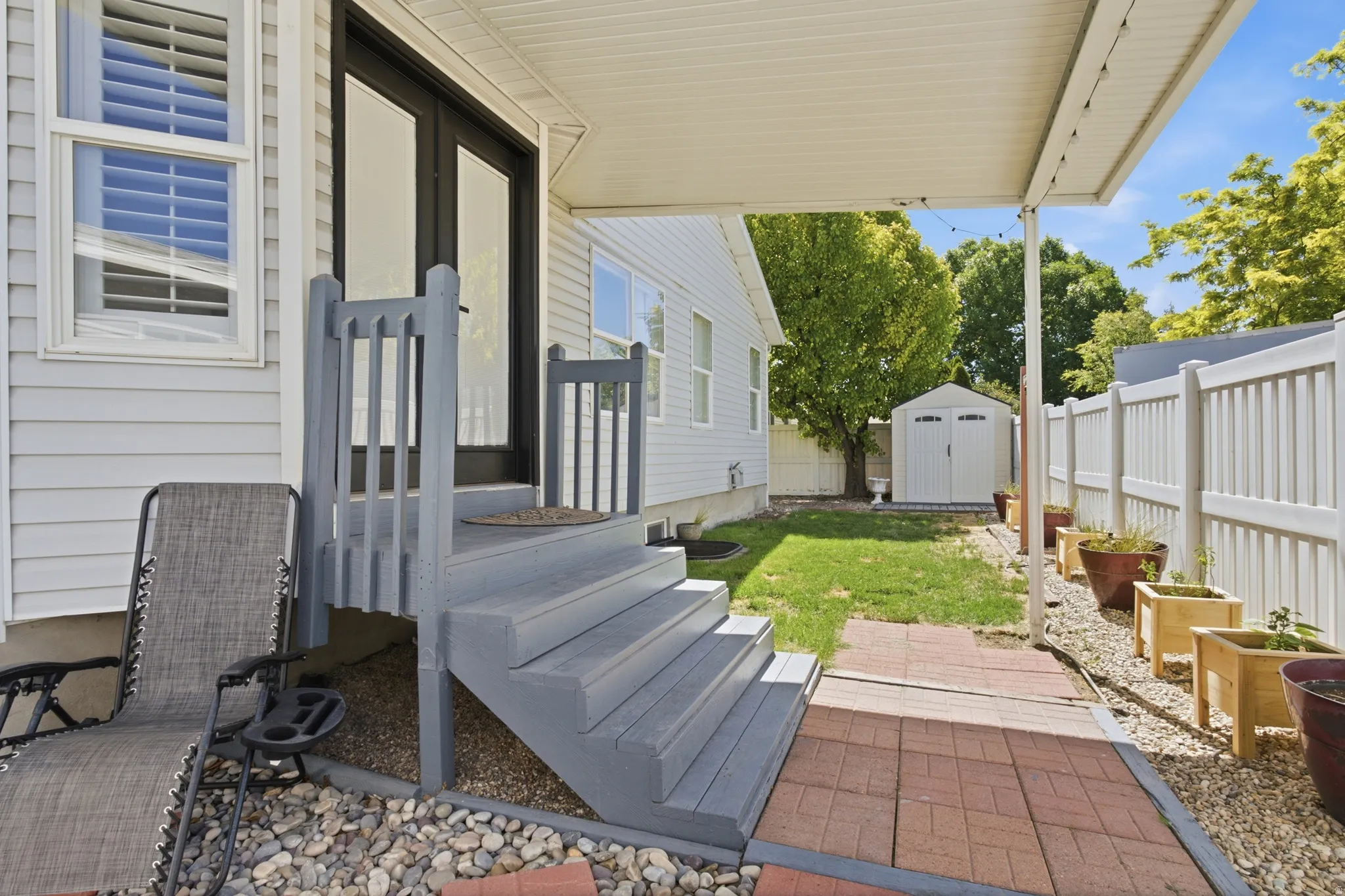Backyard featuring a covered patio, gray stained wood steps, double glass panel doors, a white vinyl privacy fence, and a storage shed (tenant's use)