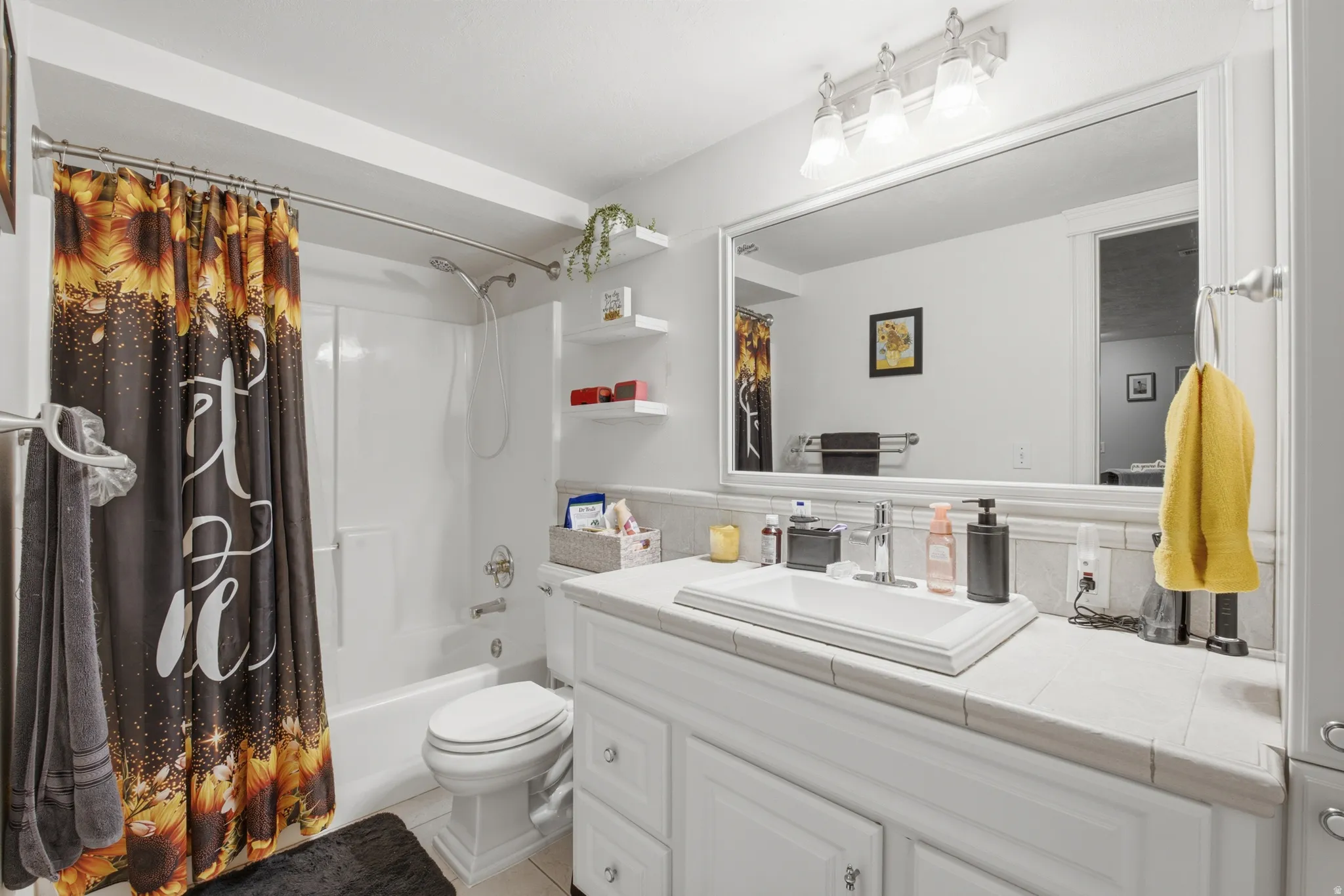 Bathroom vanity featuring a rectangular inset sink, tile countertop, and a wall-mounted mirror with overhead lighting