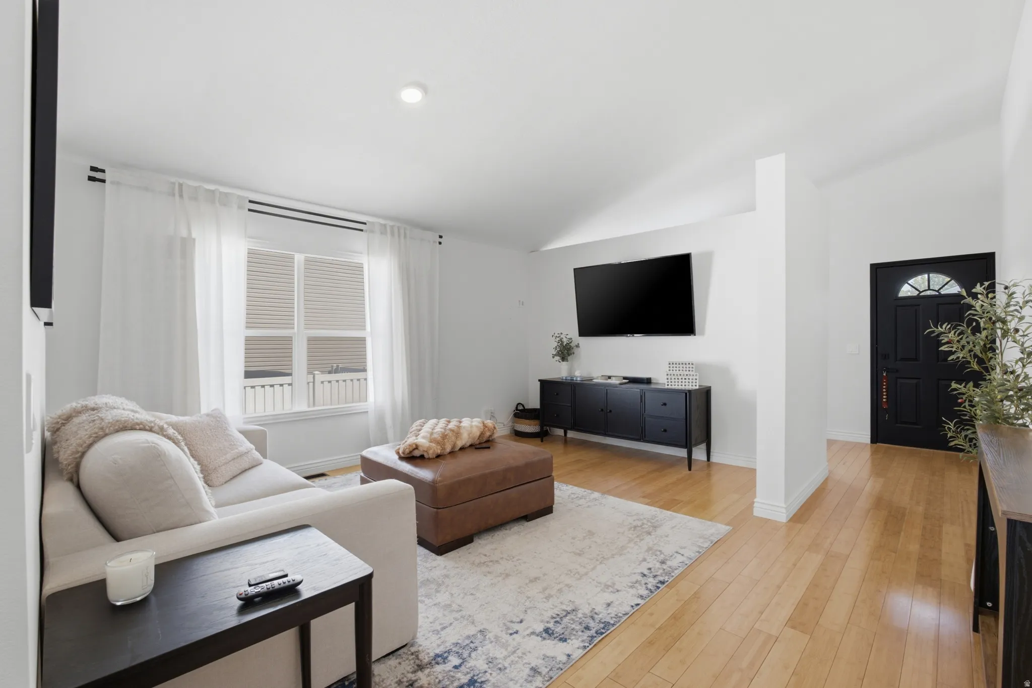 Bright living space featuring natural light, wood-finish flooring, recessed lighting, a vaulted ceiling, and a prominent entry door with an arched glass insert