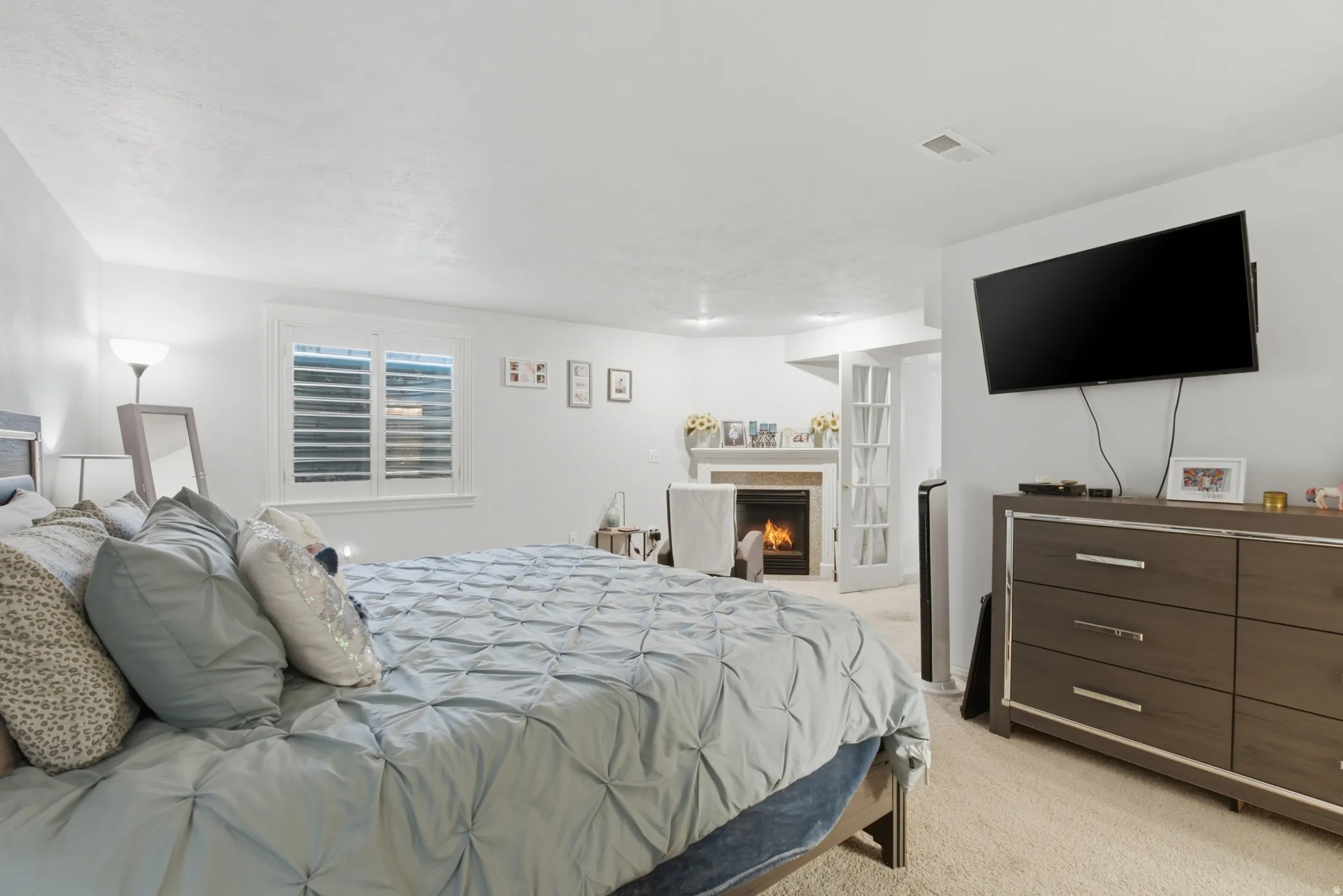 Carpeted room featuring a fireplace with a white mantel, white plantation shutters, and French doors