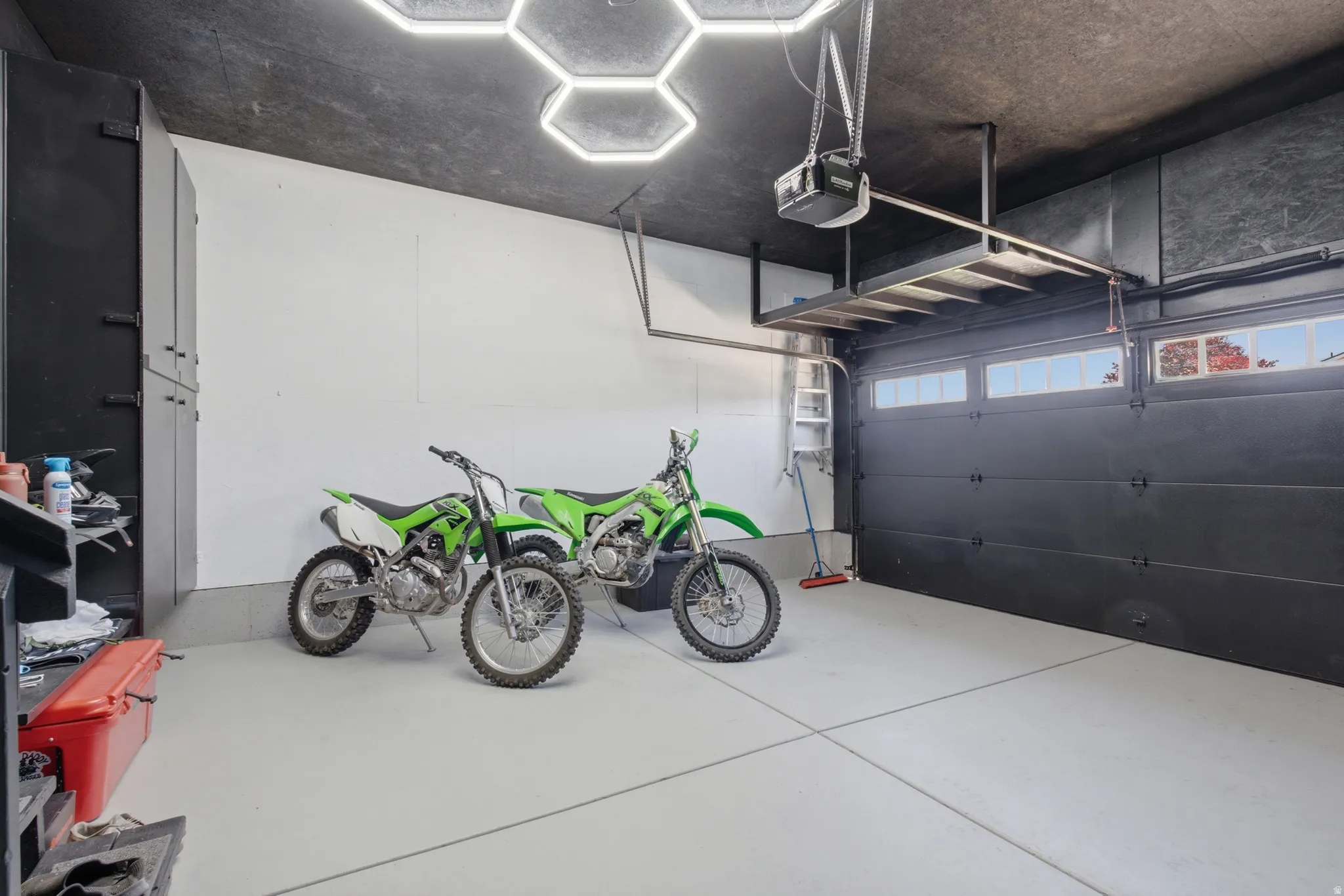 Two-car garage featuring a gray epoxy floor, hexagonal ceiling lighting, built-in black cabinetry, and an overhead storage rack