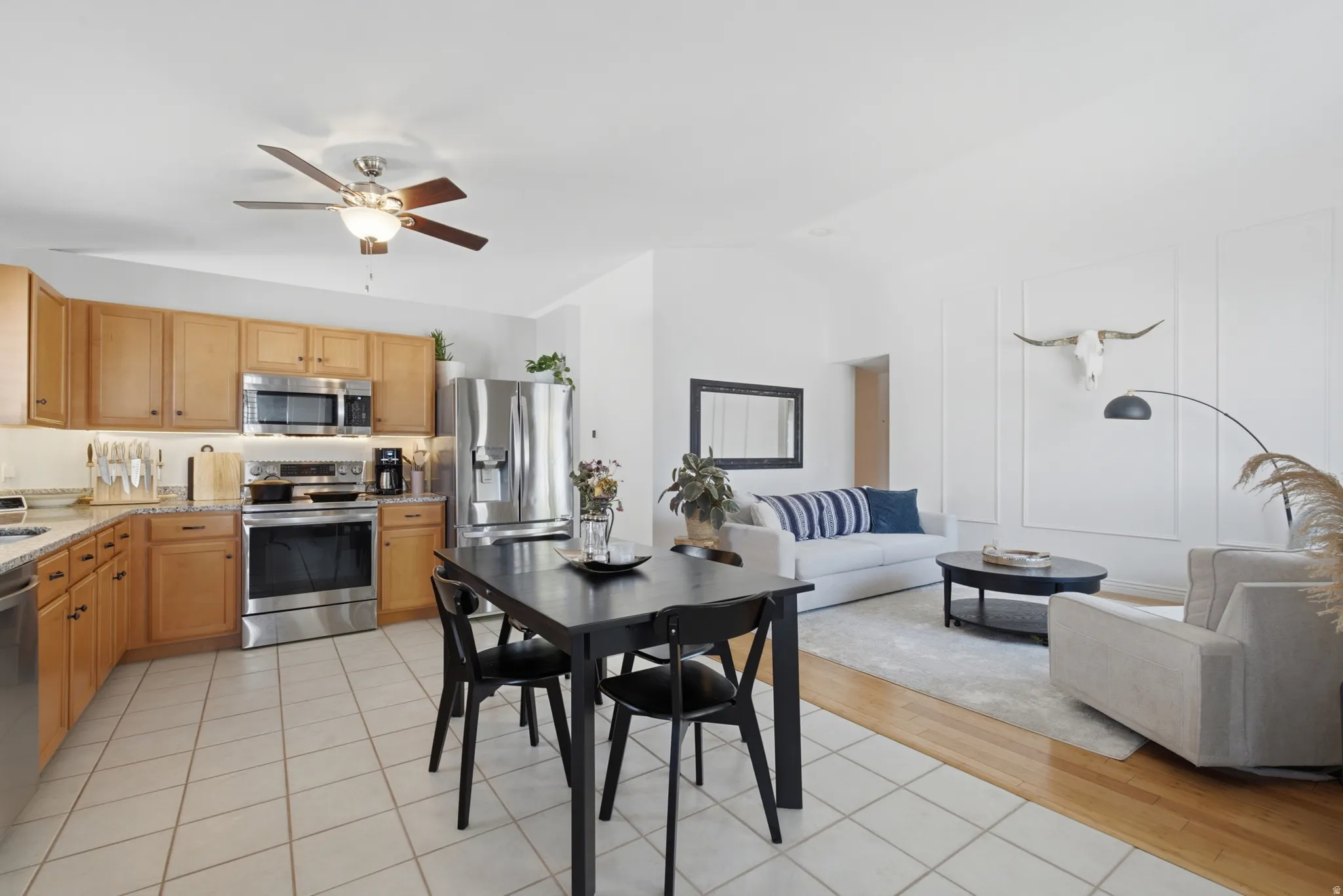 Open-concept living space featuring a kitchen with light wood cabinetry, stainless steel appliances, and tile flooring