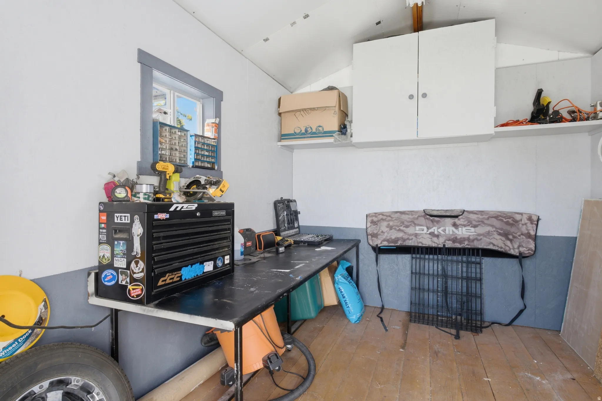 Storage shed interior with wood-finish flooring, white and gray painted walls, and an overhead window