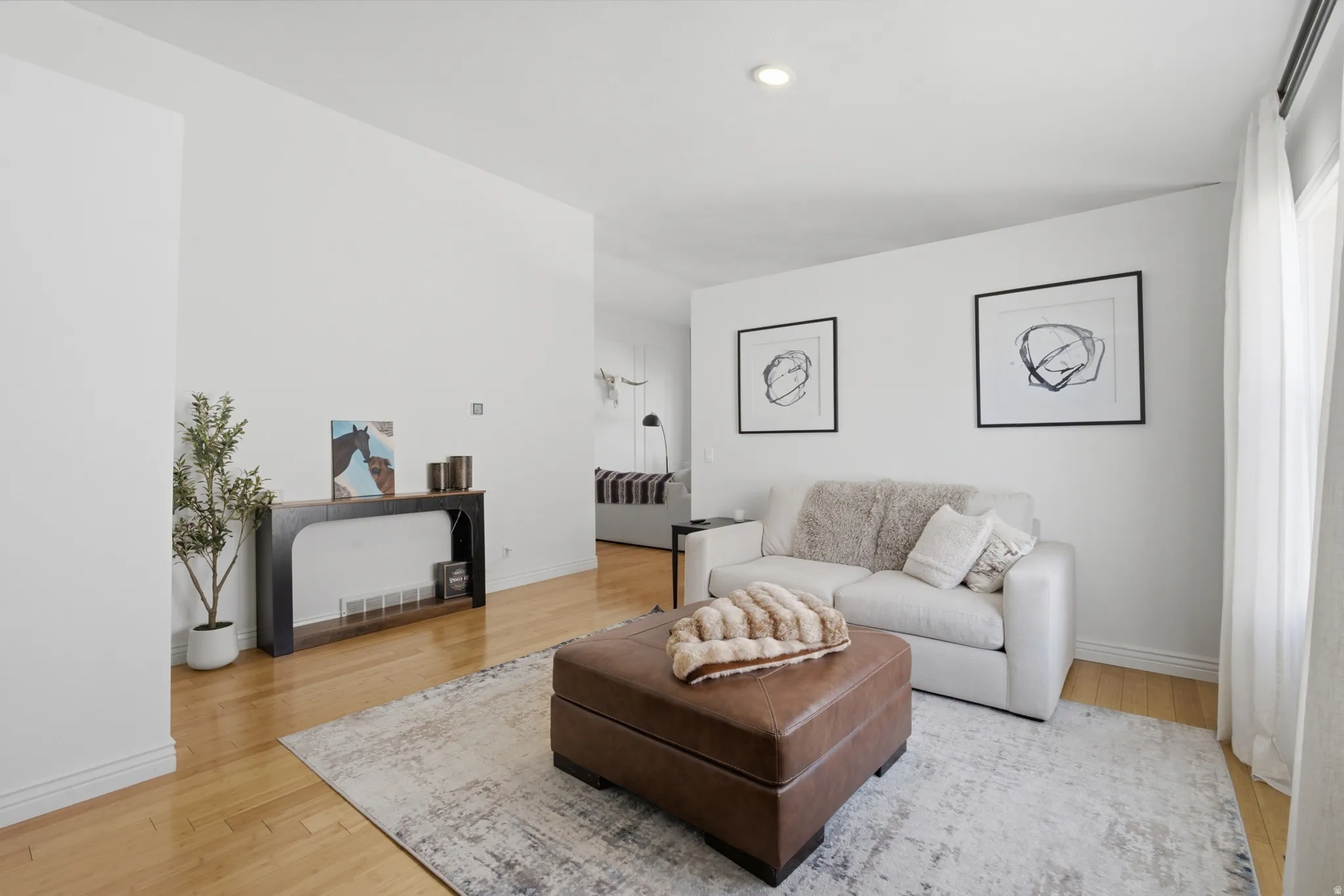 Open-concept living space featuring light wood-finish flooring, recessed ceiling lighting, a tall window with drapes, and white walls
