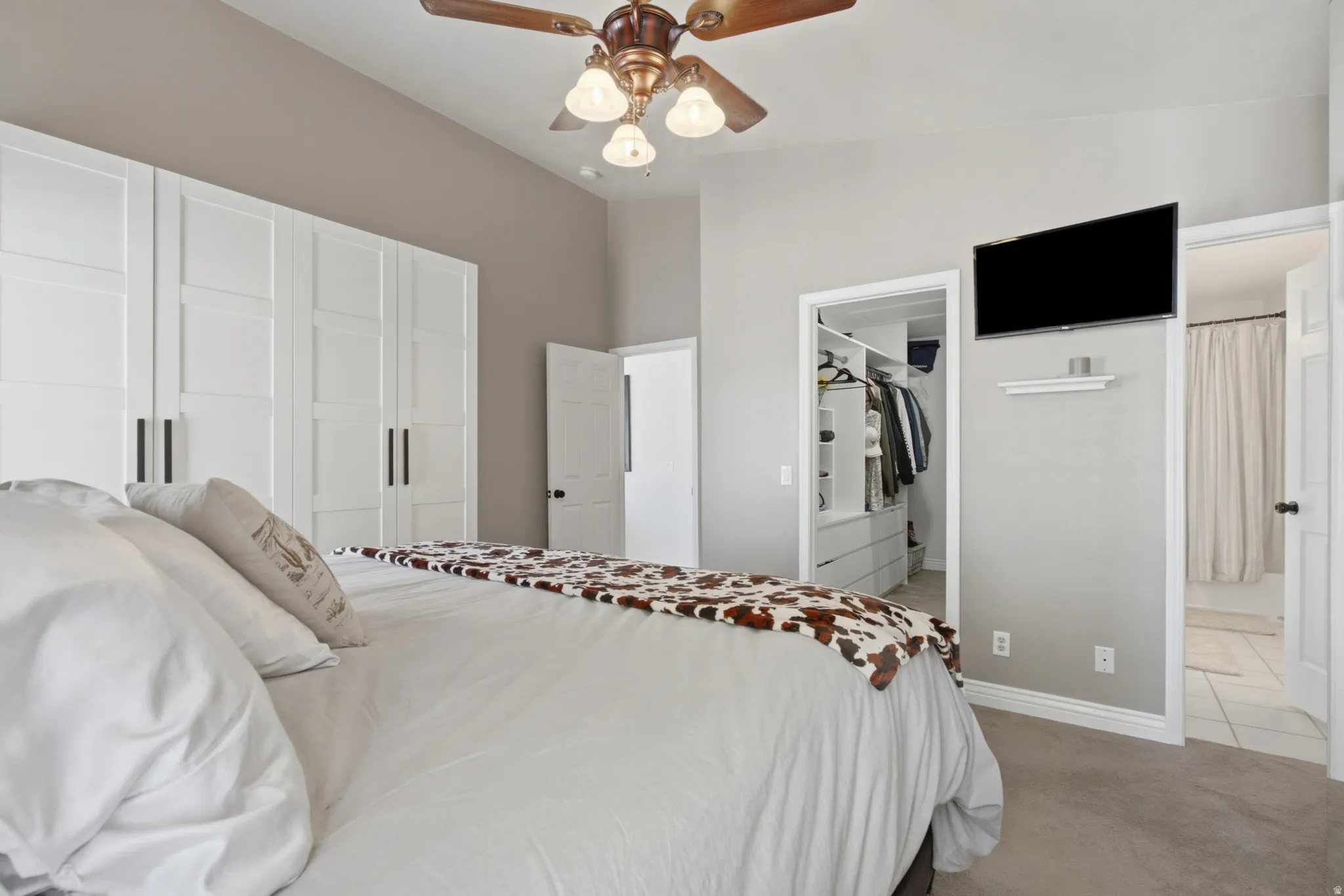 Bedroom featuring white paneled built-in wardrobes, a ceiling fan with integrated lighting, and neutral carpeting