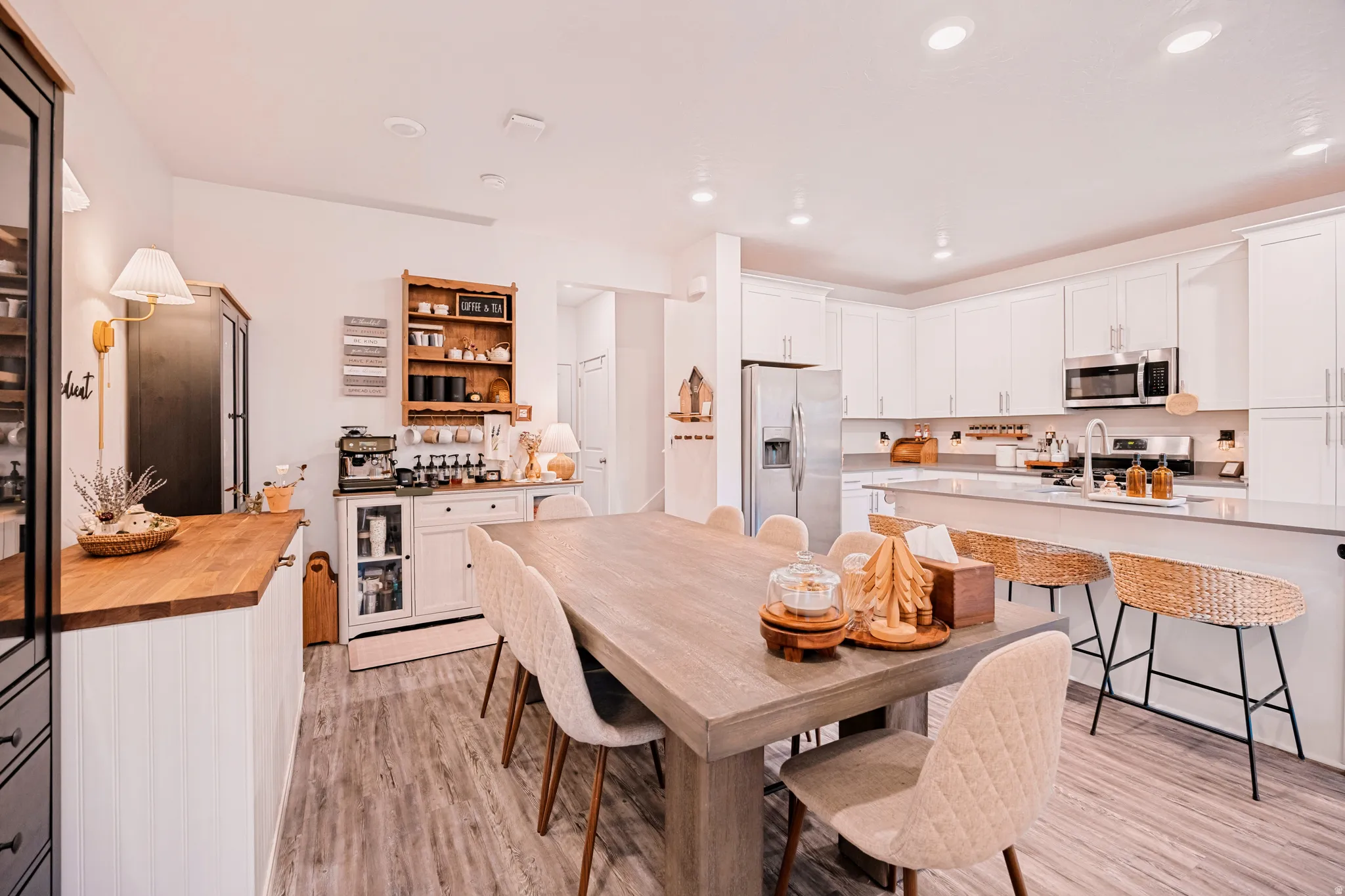 Open-concept kitchen and dining area featuring a spacious dining table, wood-finish flooring, white cabinetry, integrated stainless steel appliances, and a kitchen island with bar seating