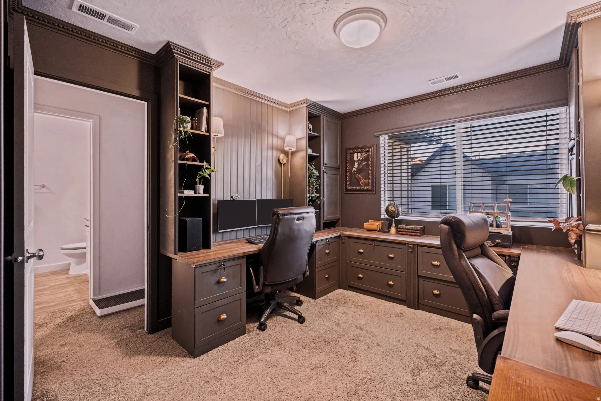 Dedicated office space featuring extensive built-in cabinetry, wood-finish countertops, wall paneling, and a window with blinds