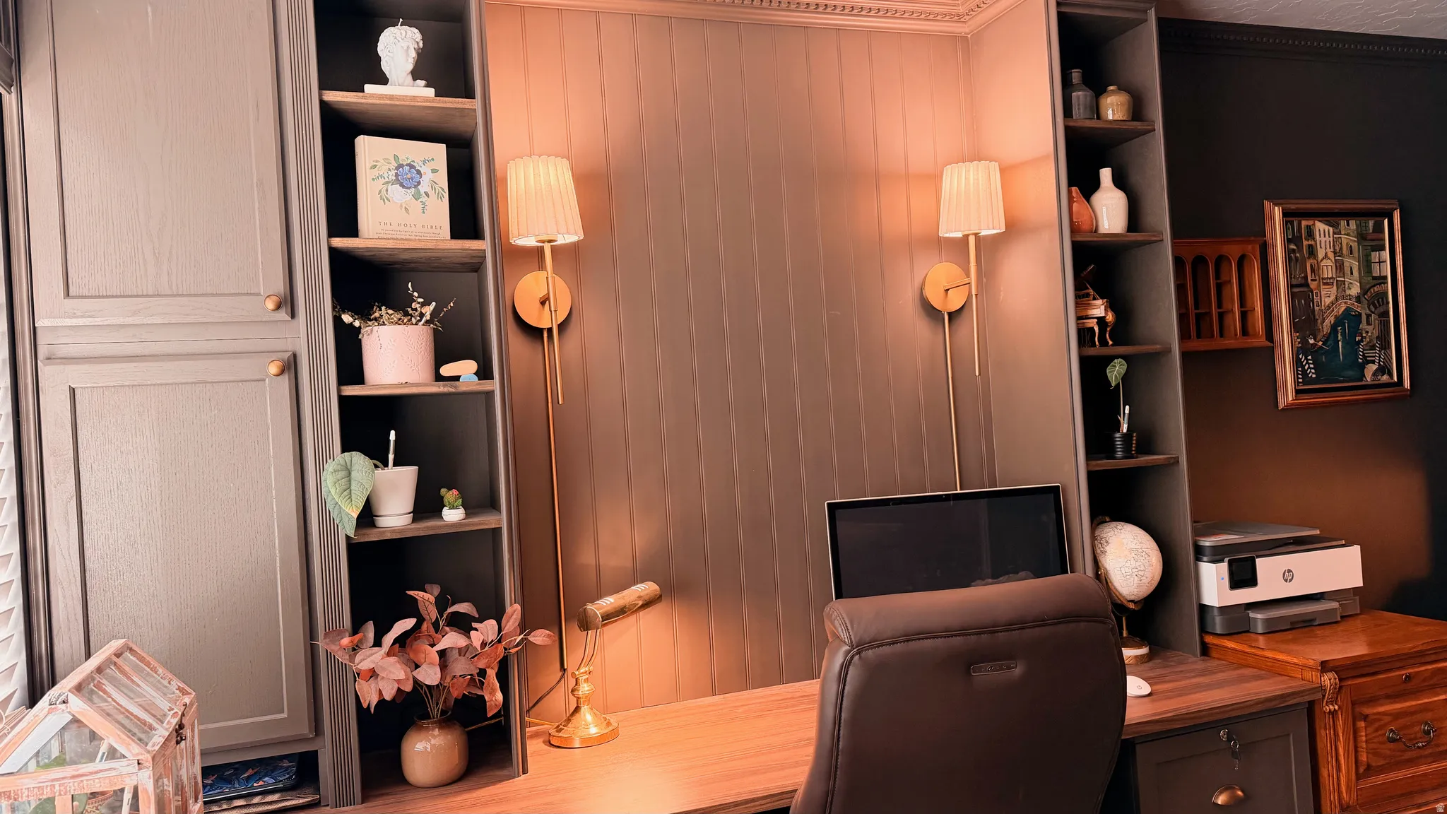 Built-in desk area featuring integrated cabinetry, open shelving, wall paneling, and two wall-mounted sconces