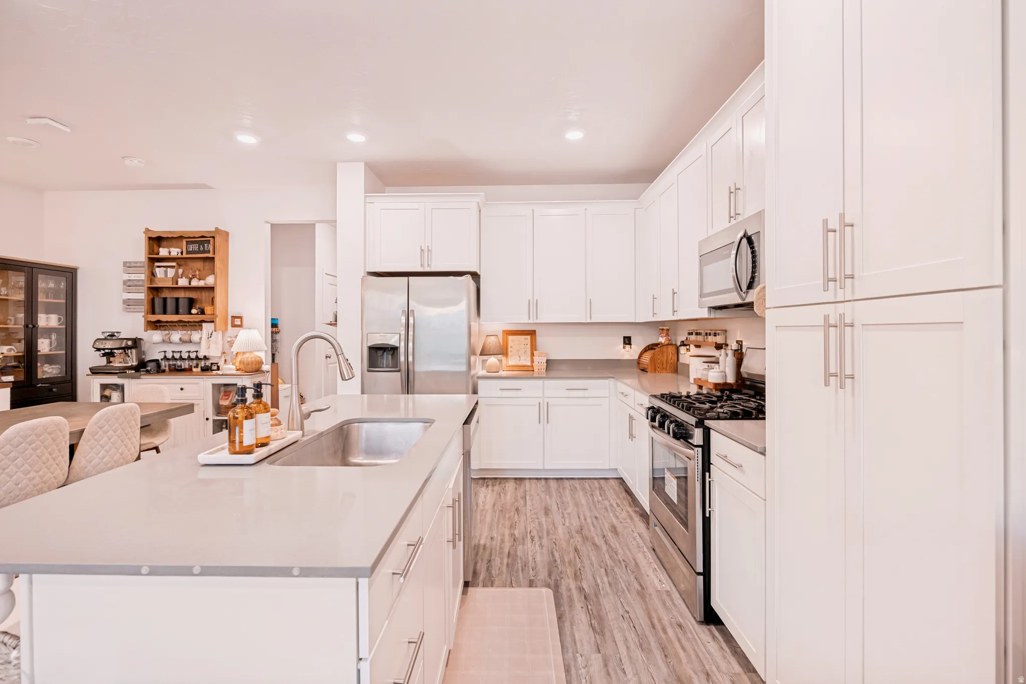 Spacious kitchen featuring white cabinetry, stainless steel appliances, a large center island with an undermount sink, light-toned countertops, and wood-finish flooring