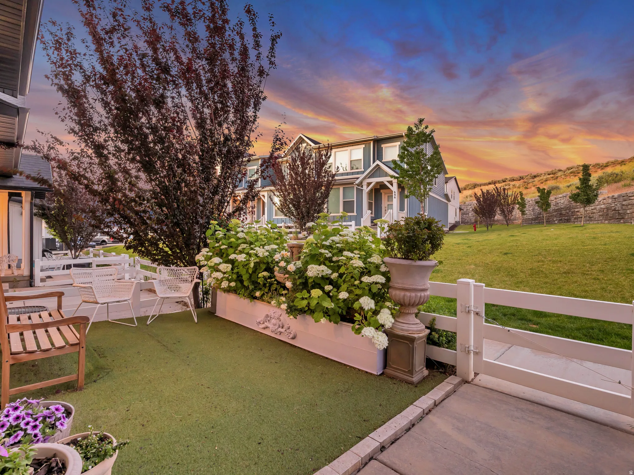 Exterior patio featuring artificial turf, a white planter box with flowering shrubs, and a white picket fence