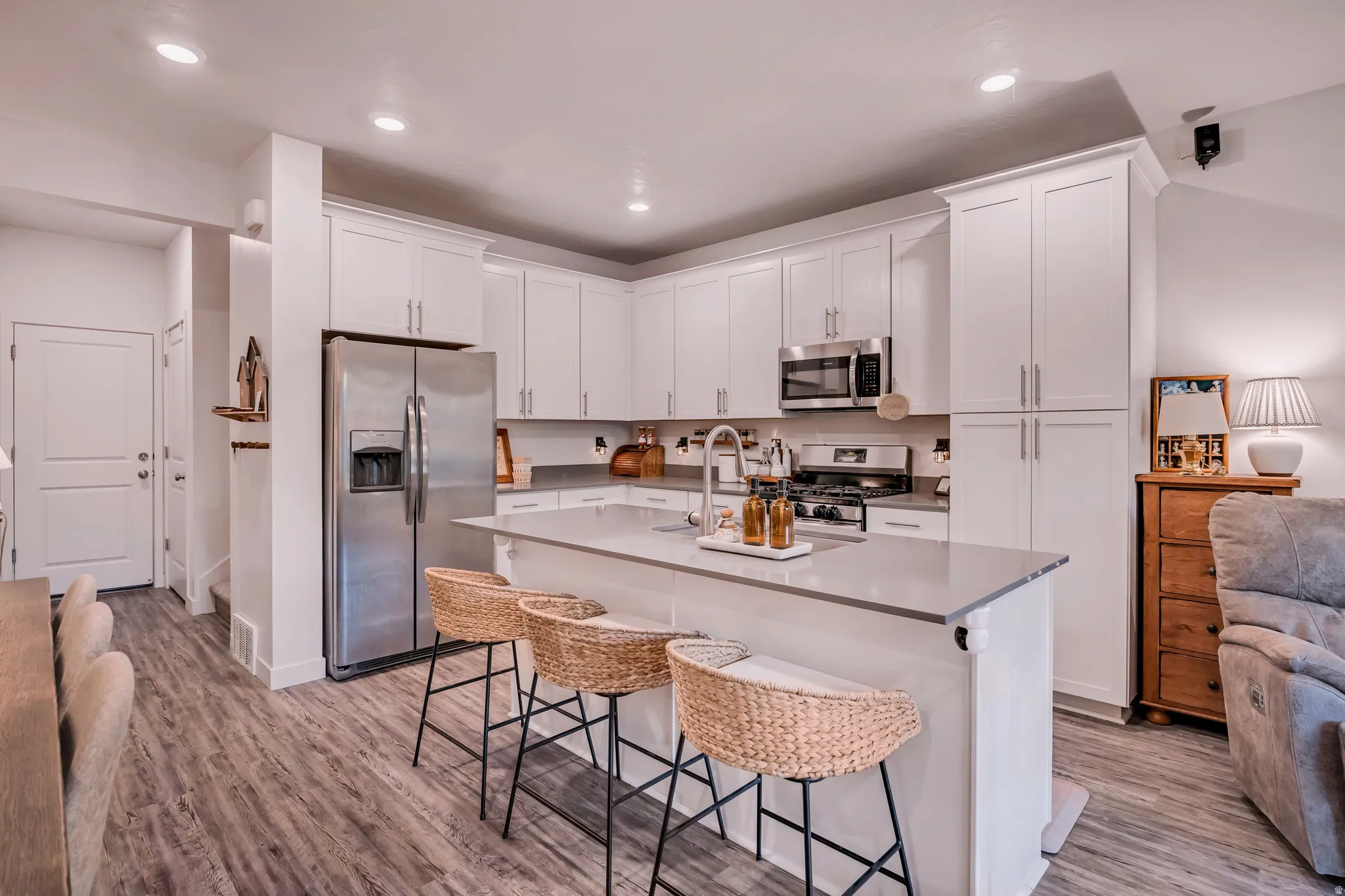 Contemporary kitchen featuring white shaker cabinetry, stainless steel appliances, a large center island with seating, and wood-finish flooring
