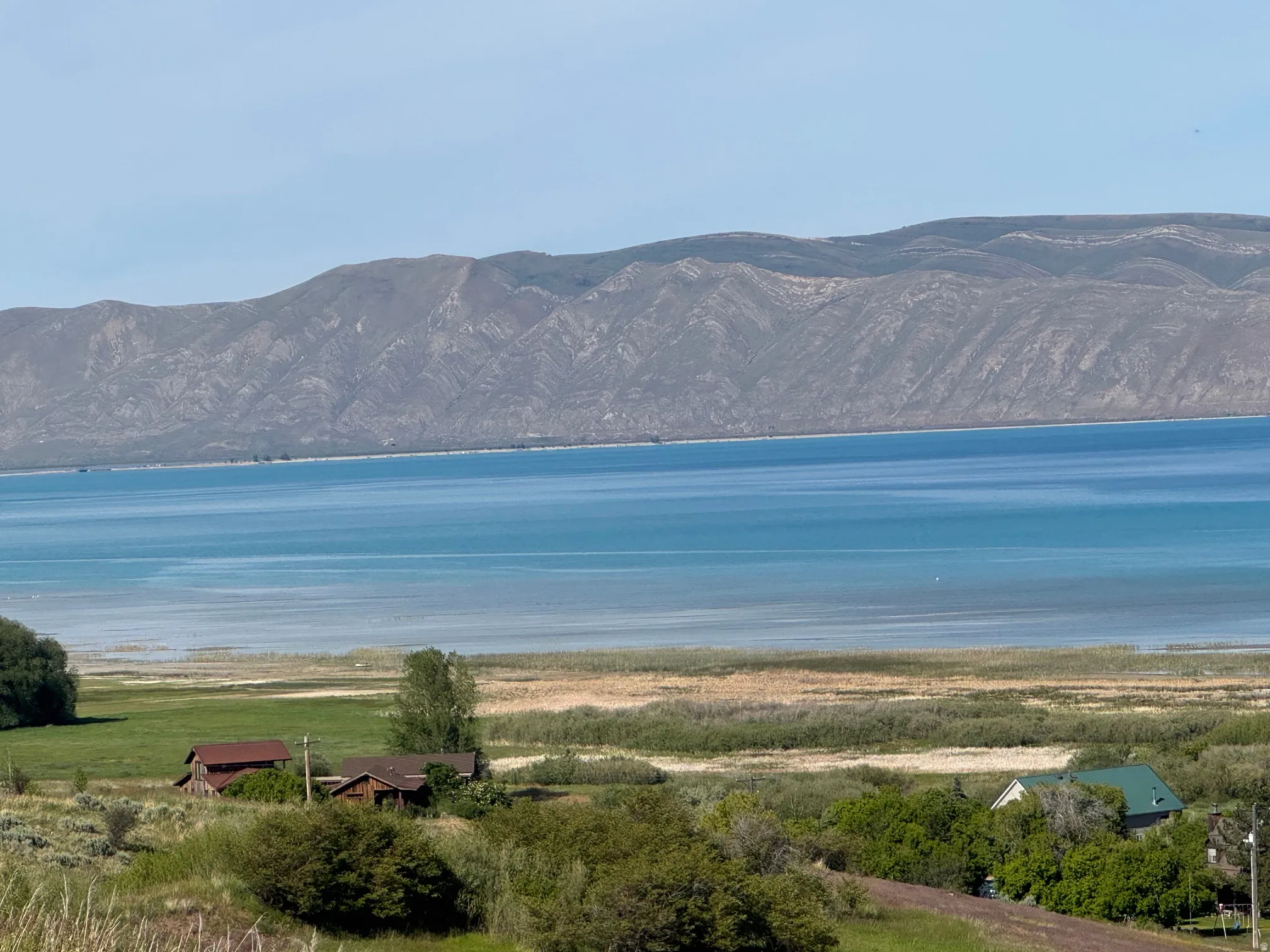 Expansive waterscape featuring a large body of water with a distinct shoreline, backed by substantial mountain ranges