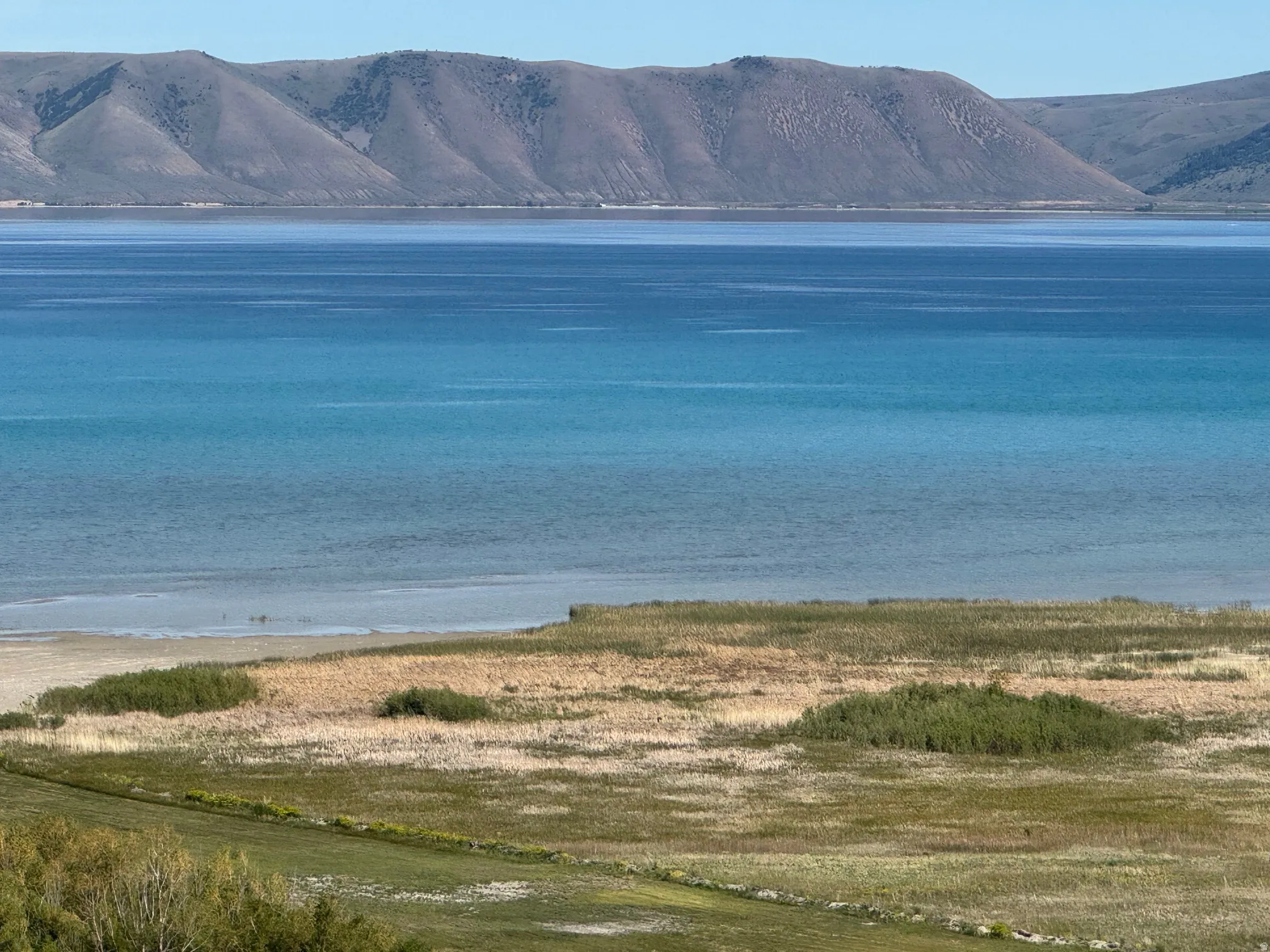 Expansive water body with varying blue hues and distant rolling hills