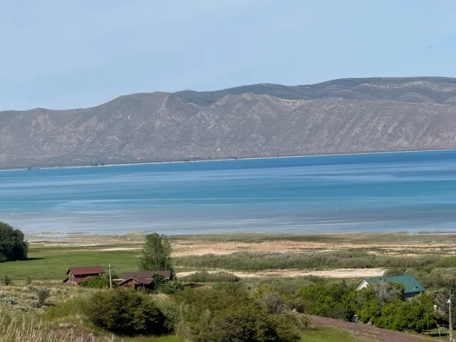 Expansive waterscape featuring a large body of water with a distinct shoreline, backed by substantial mountain ranges