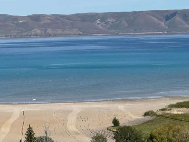 Expansive waterfront property featuring a sandy beach, serene blue water, and distant mountain landscape